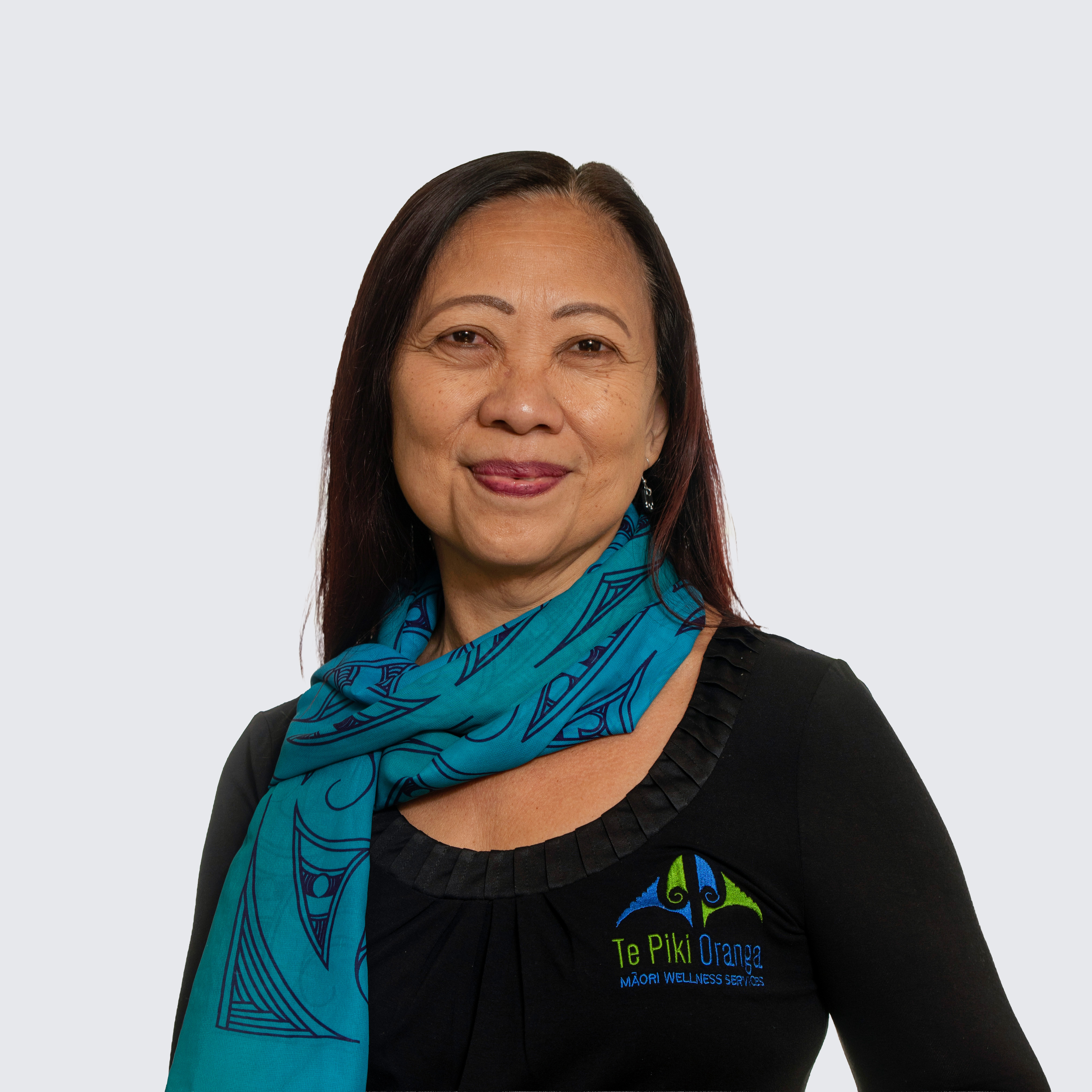 A woman with long brown hair, glasses, and a black top, smiling against a light background.