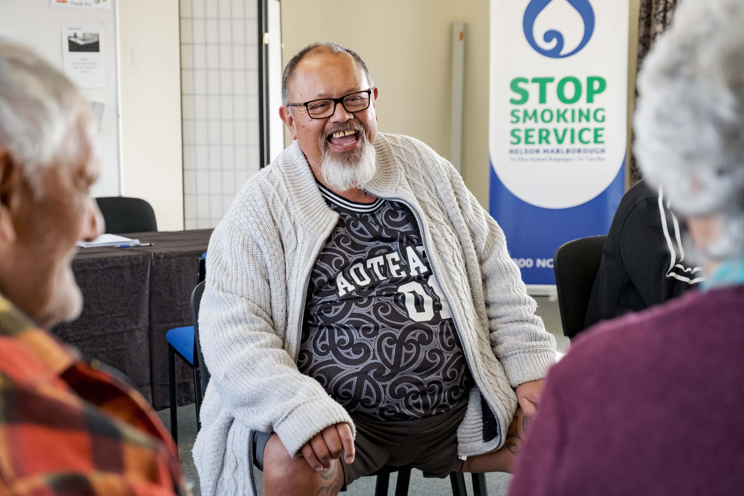 A group of elderly people sitting in a circle, smiling and talking during a support group meeting.