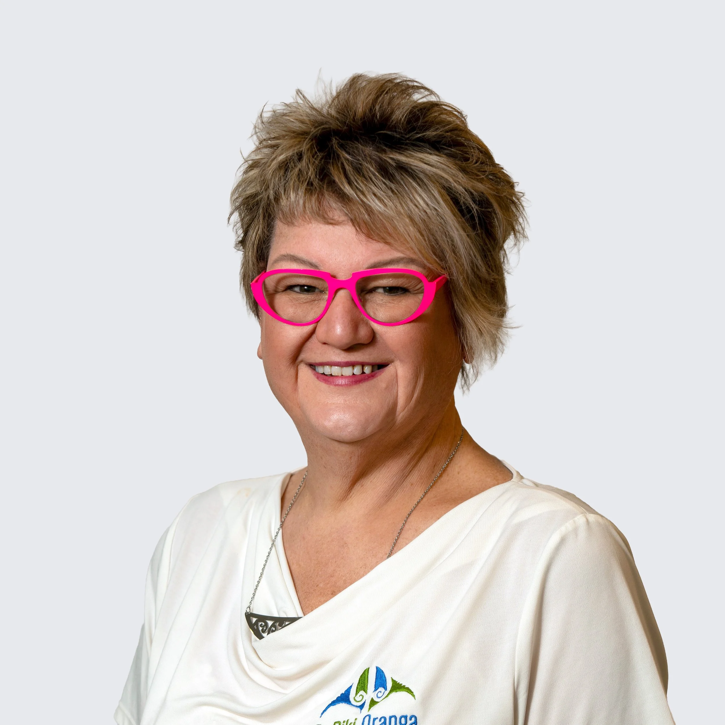 A woman with short curly brown hair, glasses, and a blue patterned scarf smiling against a plain background.