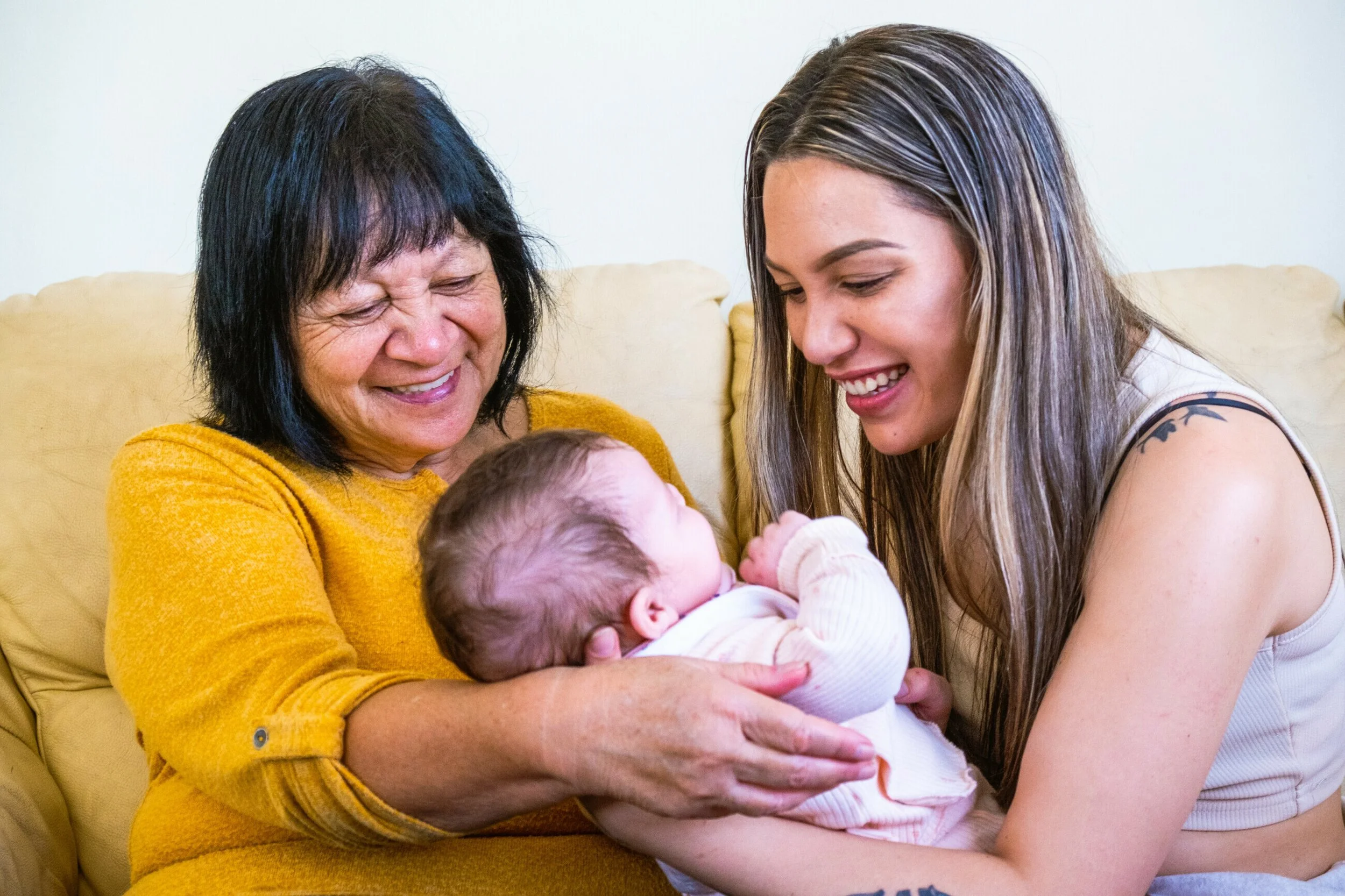 Three women, including an elderly woman, a young woman, and a baby, sharing a joyful moment together in a living room.