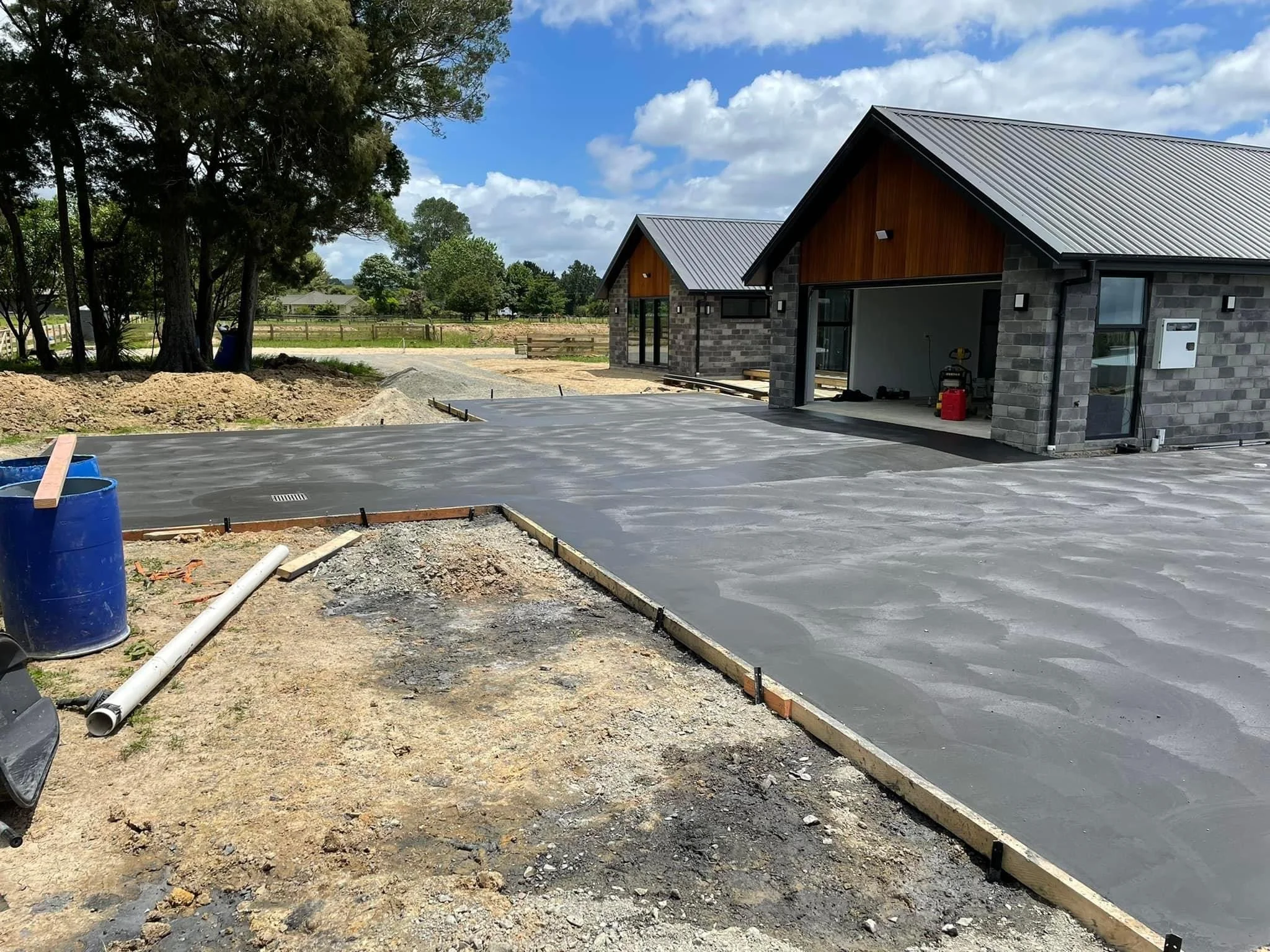 Newly poured concrete driveway in front of a house under construction, with a parking area and a garage opening.