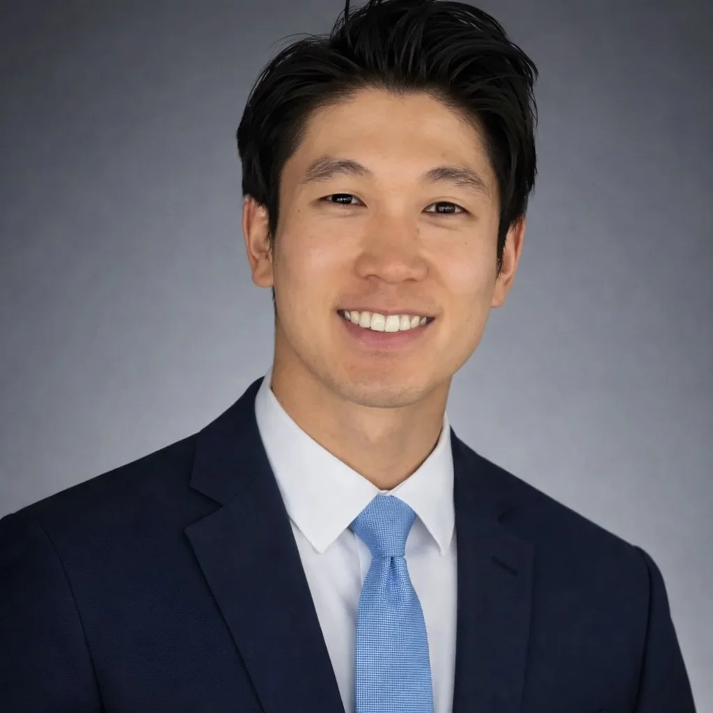 A young man in suit and tie smiling in front of a brick wall background.