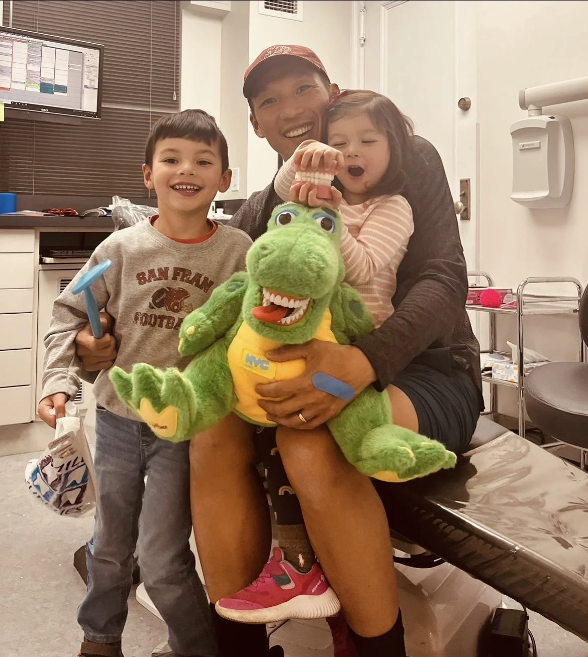 A man with two children, a boy and a girl, posing with a Dr. Roar stuffed animal in a medical examination room.