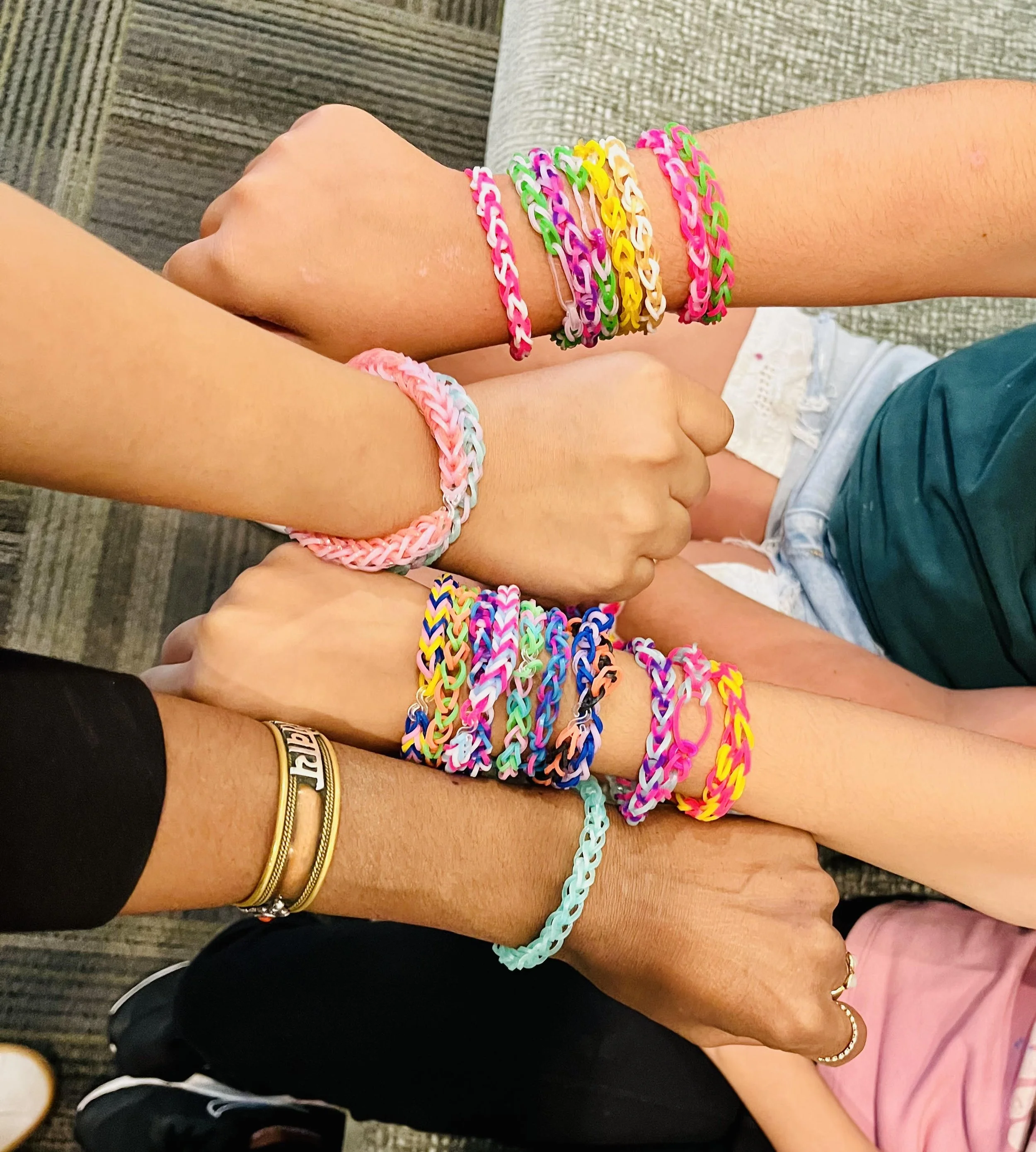 Multiple arms showing colorful rubber band bracelets with different designs and colors, overlapping each other.