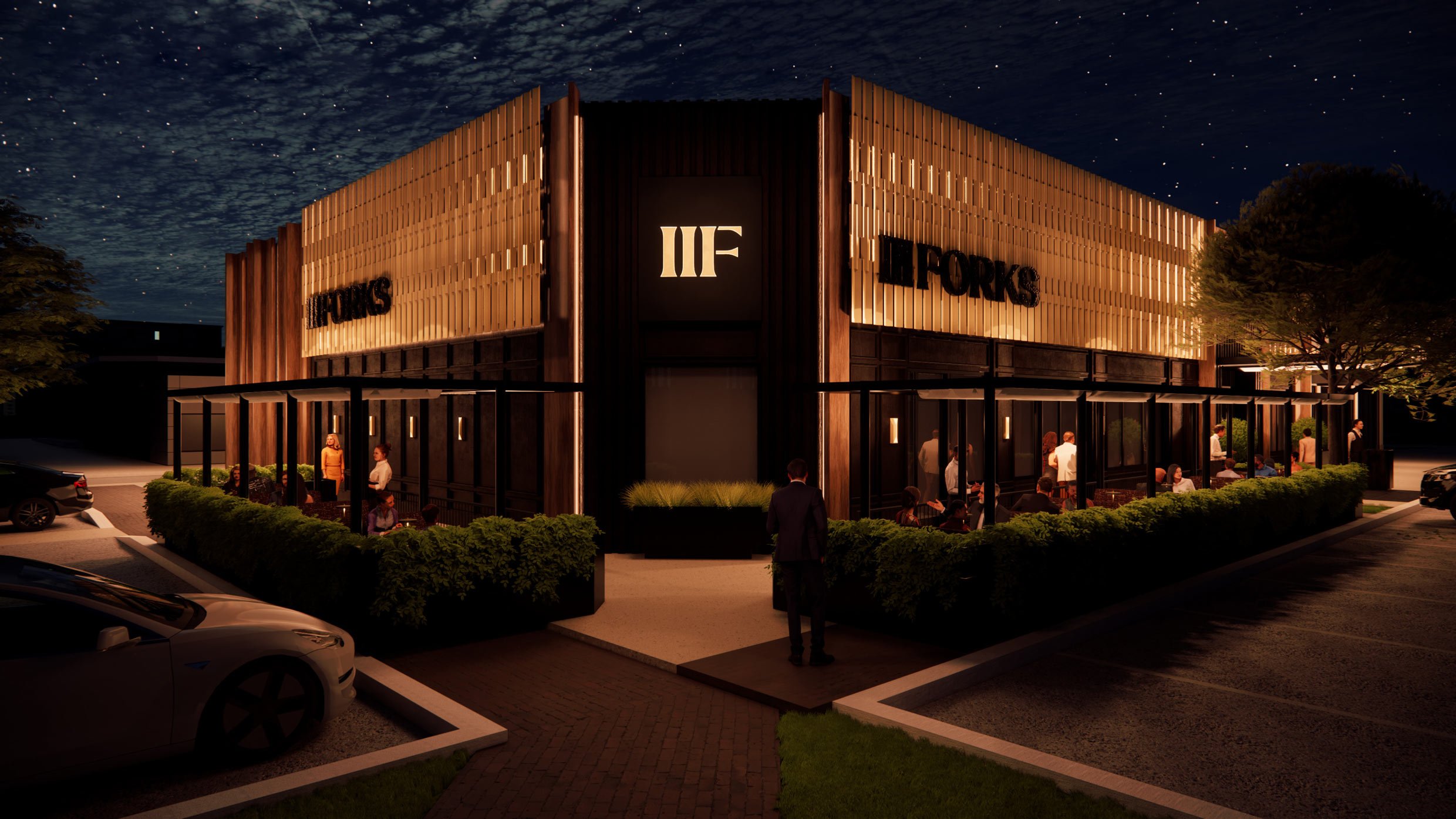 Nighttime exterior view of a modern restaurant building with large windows and outdoor seating. The building has a black and wood facade with a lit sign that reads 'ILFORKS.' People are sitting and standing outside, and cars are parked in the lot. The night sky is visible with stars.