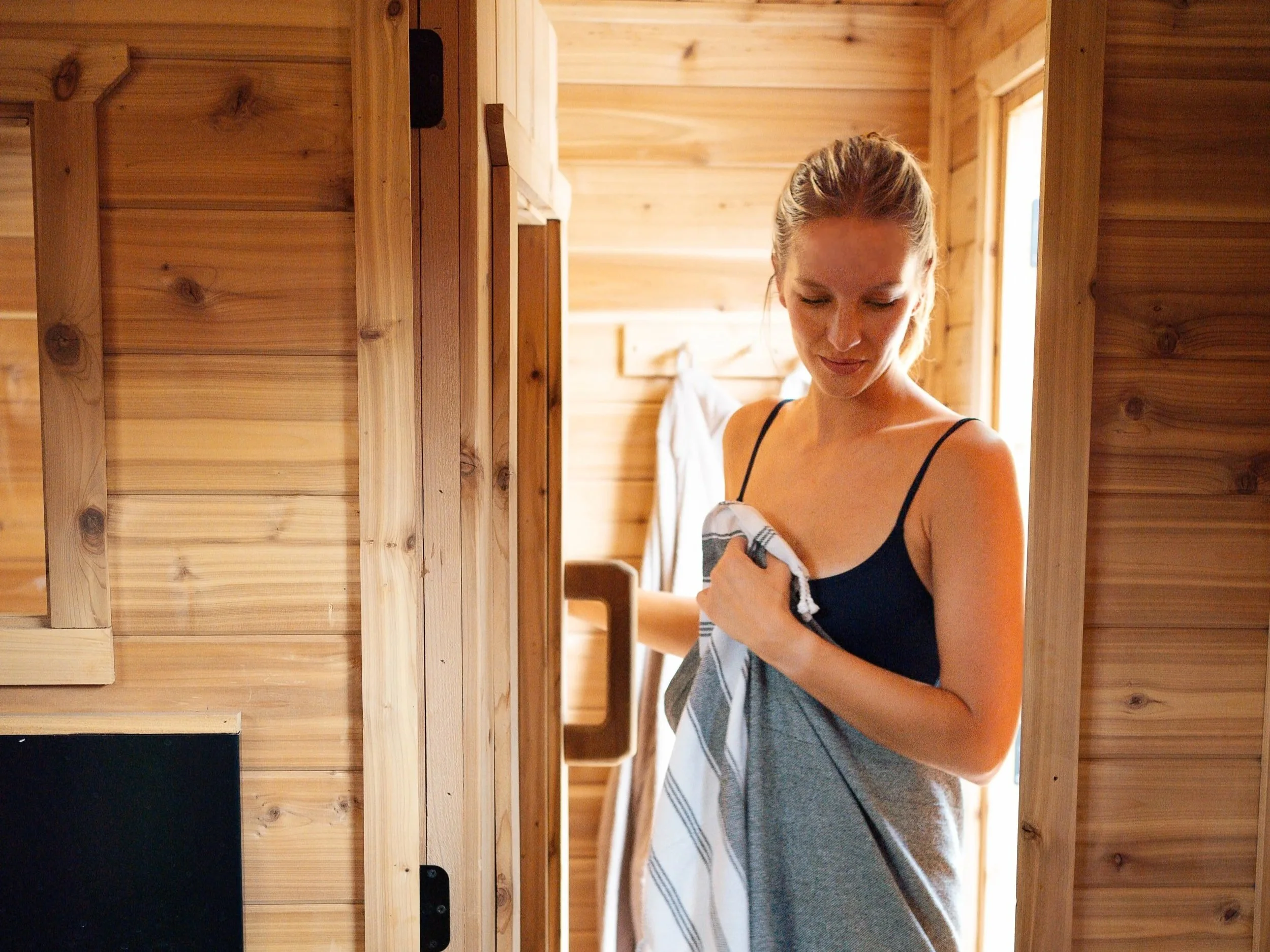 A woman with a towel wrapped around her waist and wearing a swimsuit, walking into a sauna hot room from the changeroom.