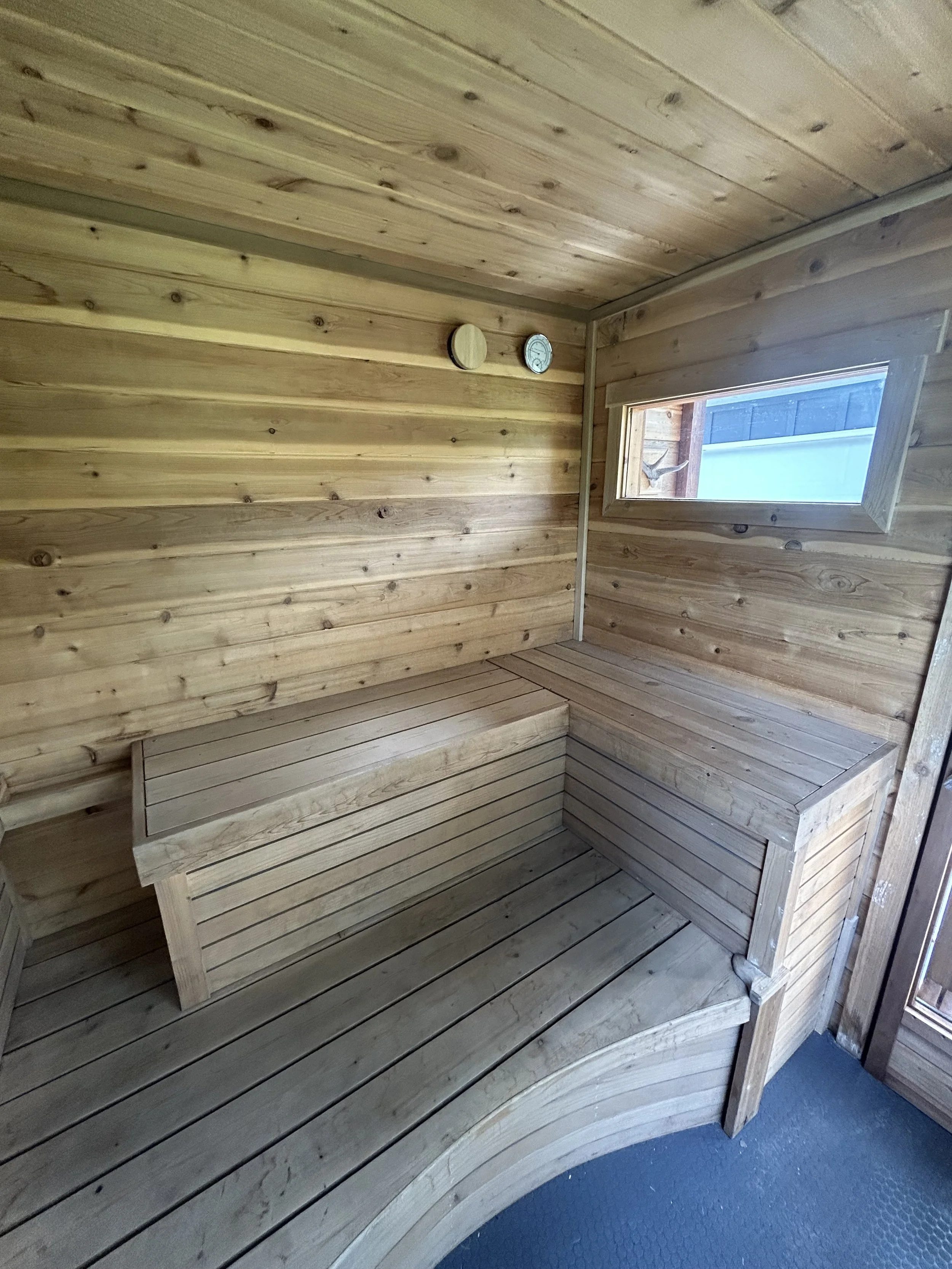 Interior of a sauna with a U-shaped bench, a transom window, and a thermometer on the wall.