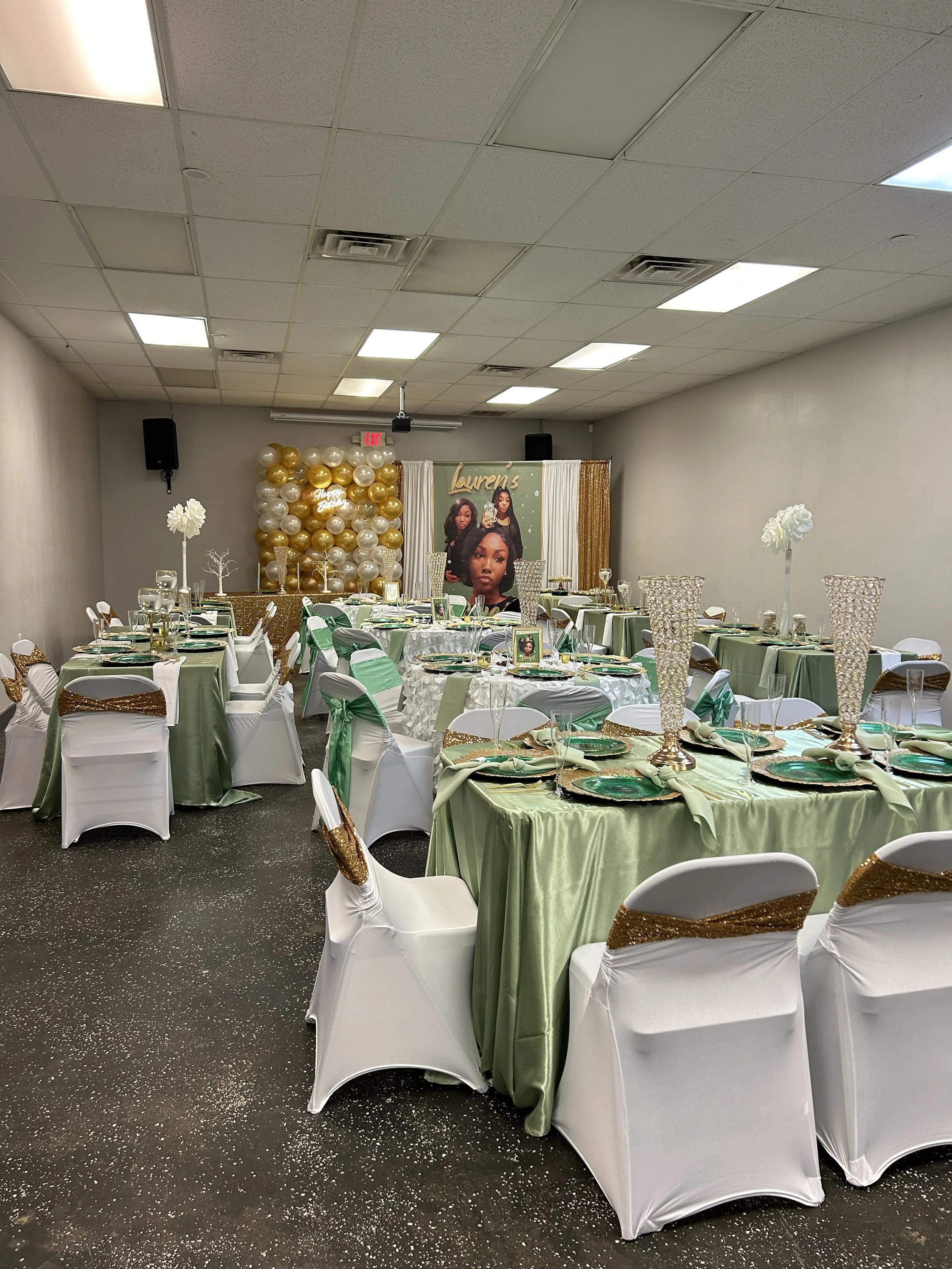 Decorated banquet hall with green and white tablecloths, white chairs with gold sashes, tall gold and white balloons, and a large poster of a woman with the name 'Lauren's' in the background.