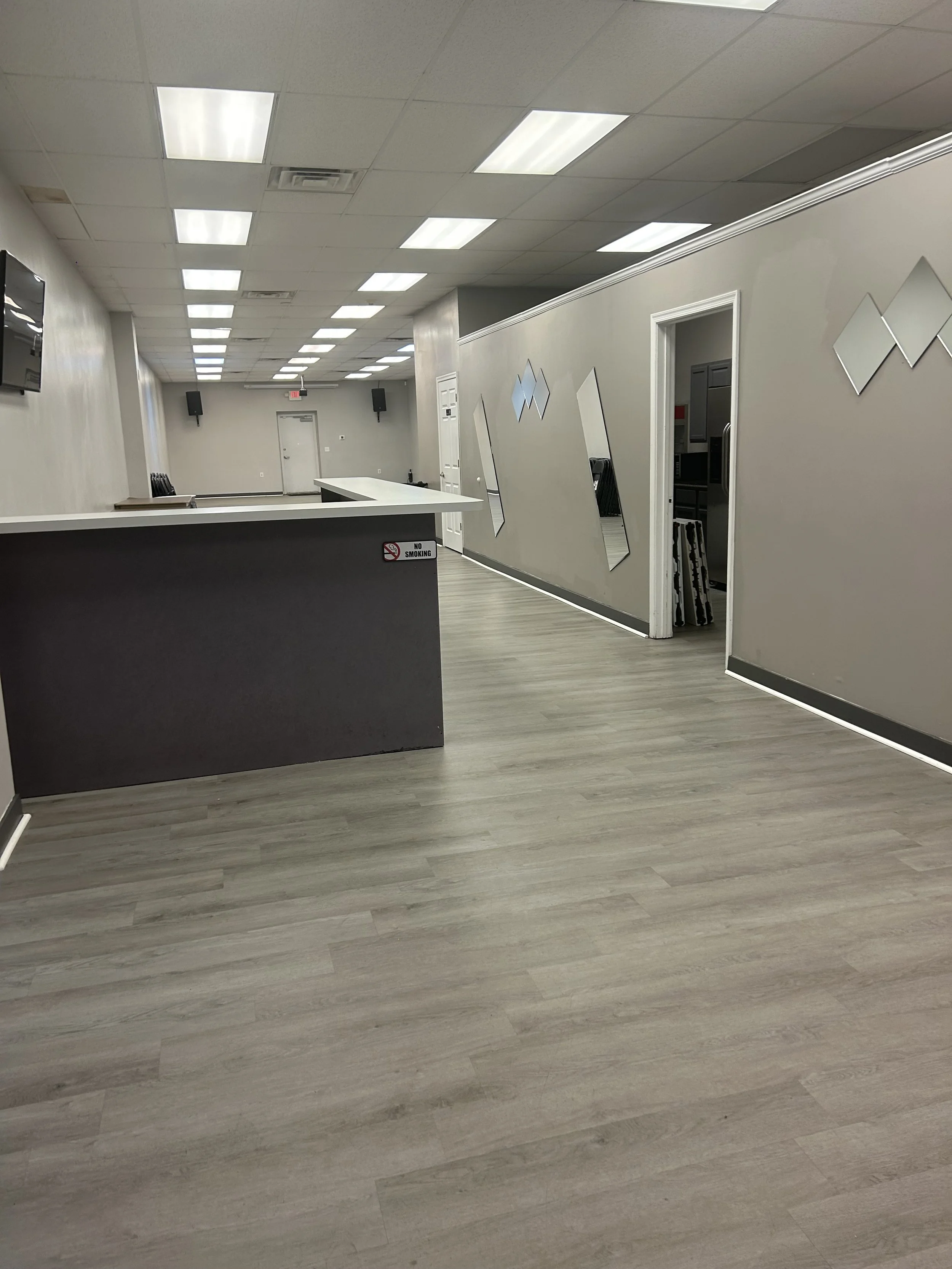 Empty lobby or reception area with a curved counter, wall-mounted mirrors, and decorative wall mirrors, with a door leading to another room.