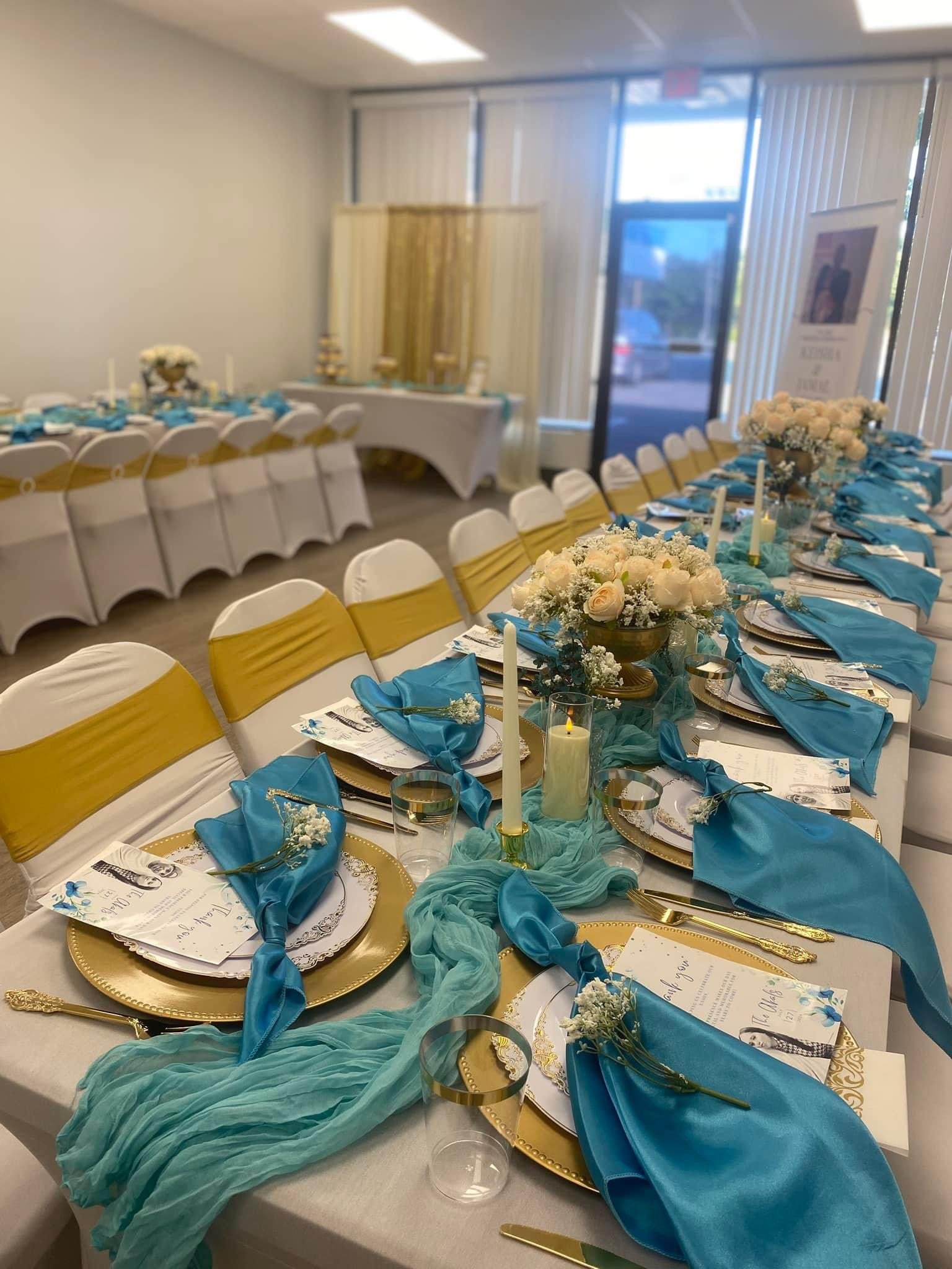 A decorated banquet table set for a wedding or special event with white, gold, and blue decor, floral centerpieces, candles, and place settings.