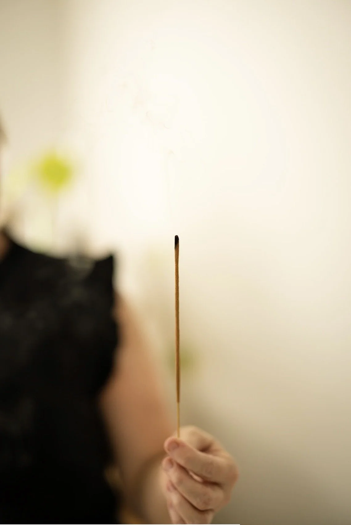 Close-up of a person holding an incense stick, with a bright but blurred magical-looking background.