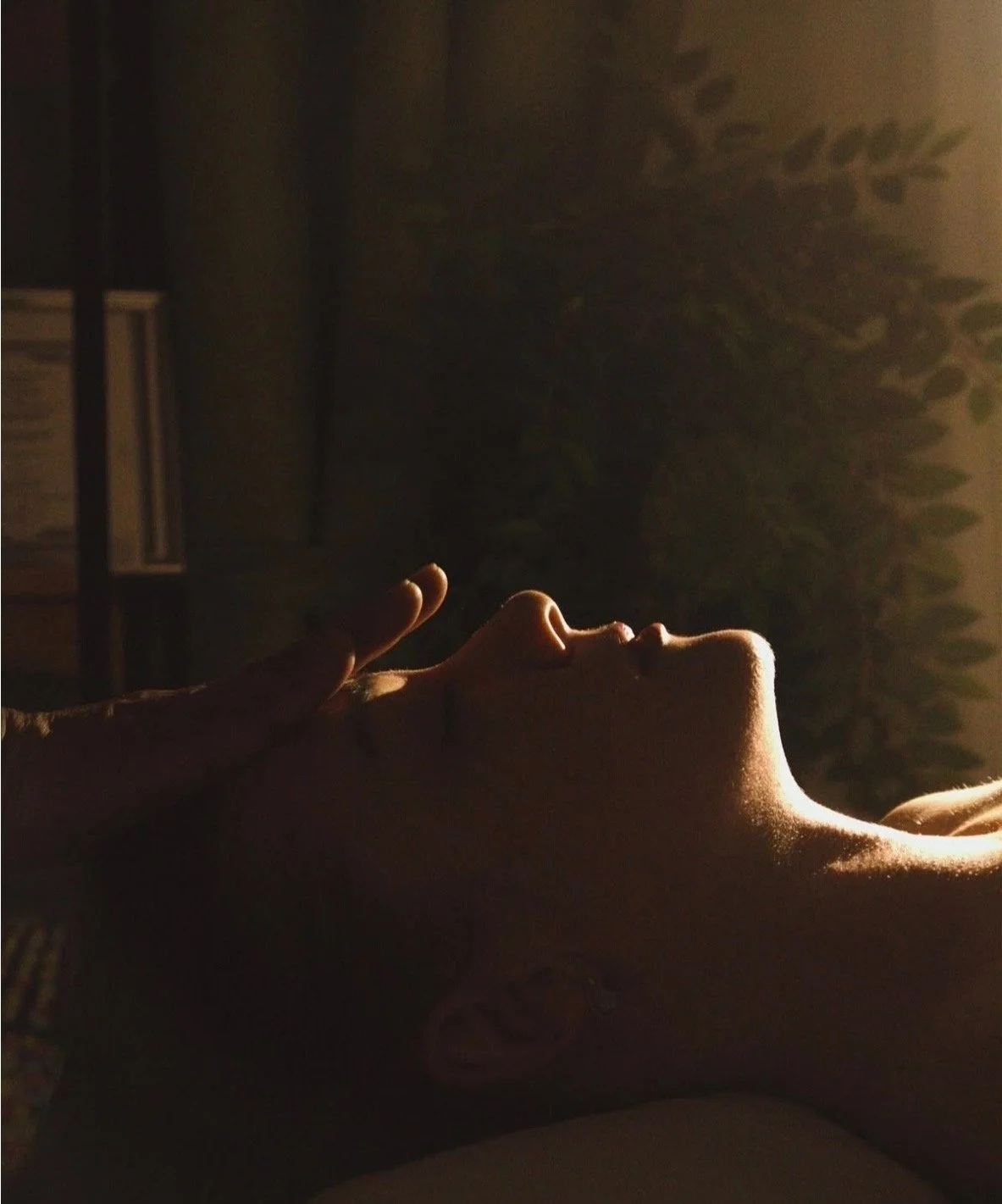 A woman lying down with her eyes closed, side to camera, illuminated by soft, warm light, her face framed by the photo.