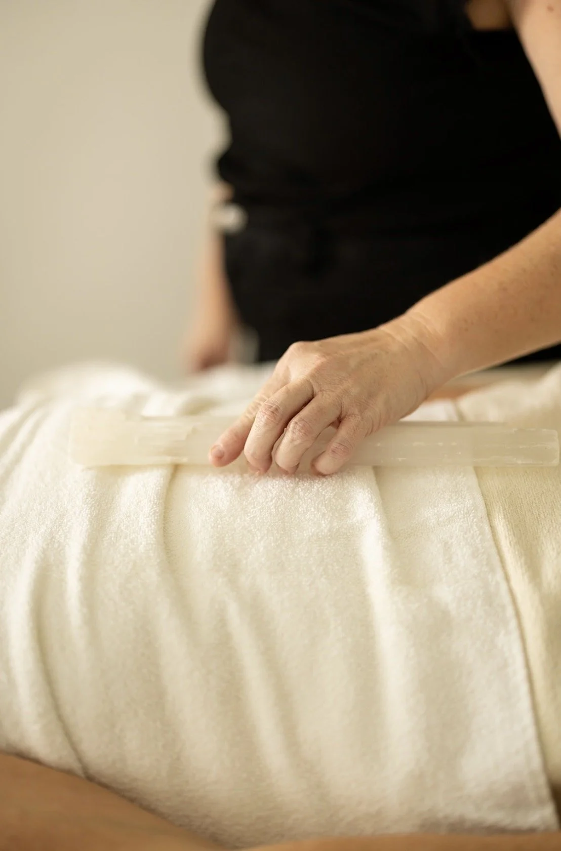 Person lying face down on a massage table, receiving a massage with their hand resting on their lower back.
