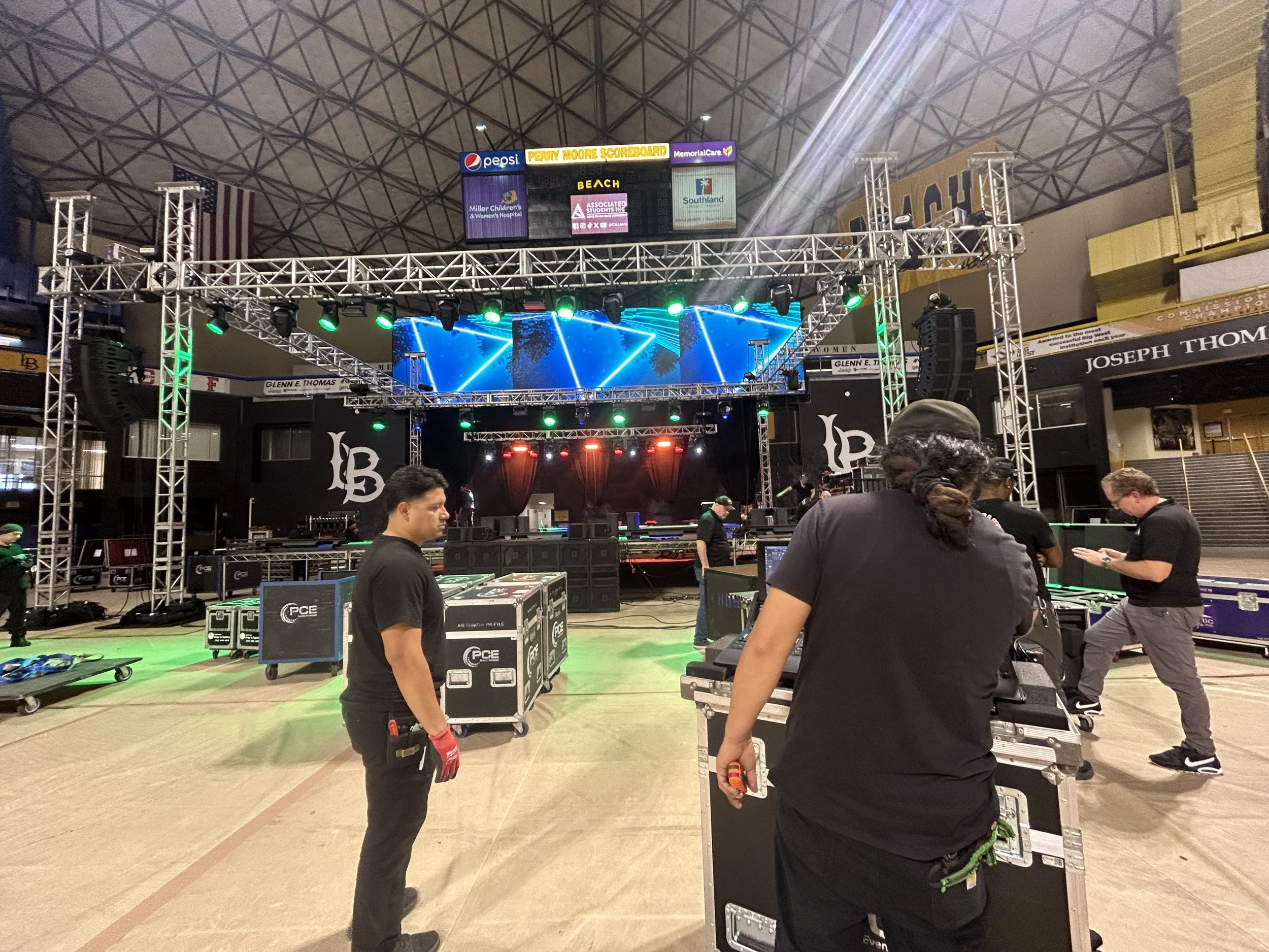 Stage being set up for a concert or event in an indoor arena with workers preparing equipment and lighting.
