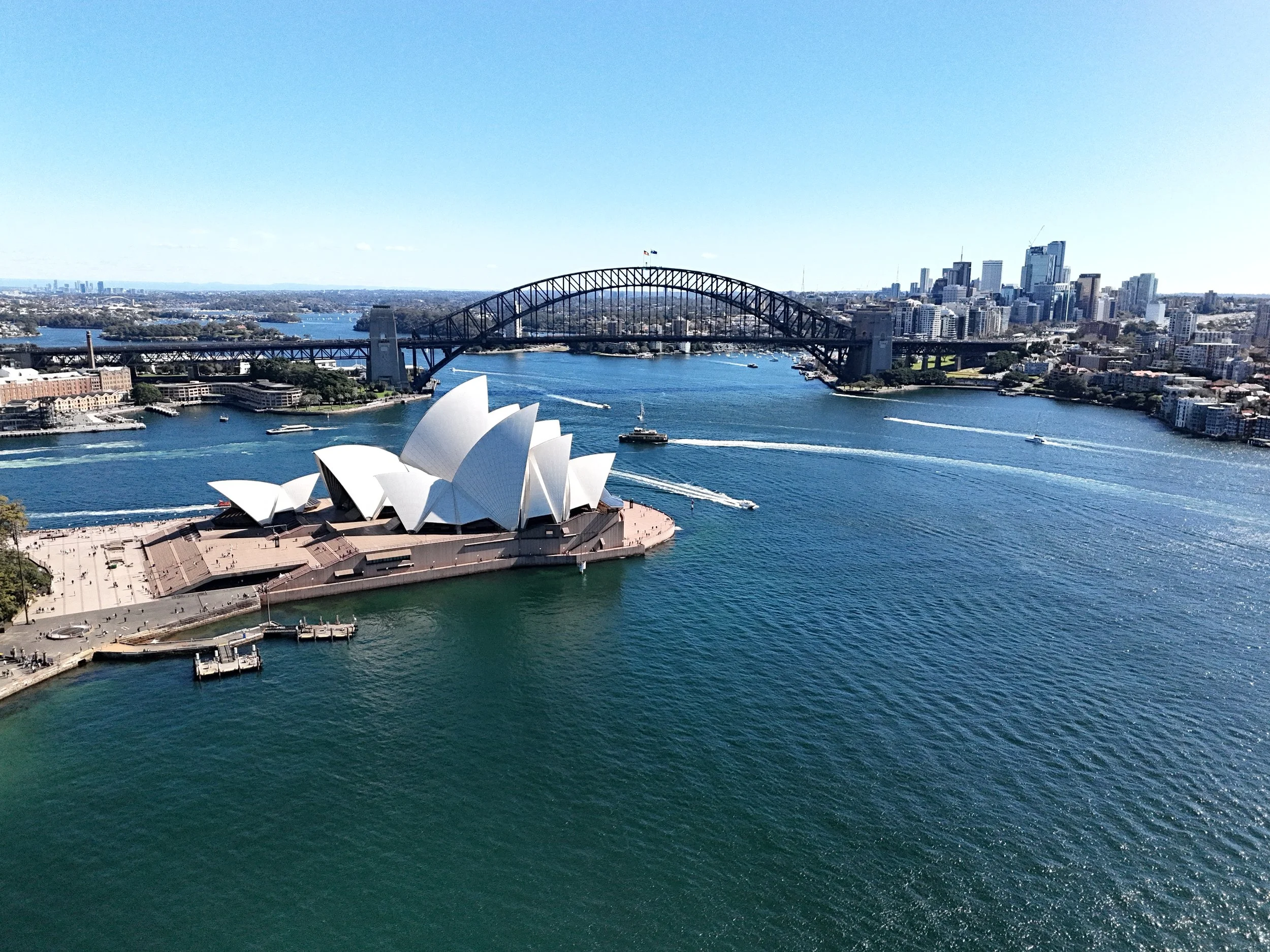 Aerial view of Sydney Opera House and Harbour Bridge with boats in Sydney Harbour on a clear day.