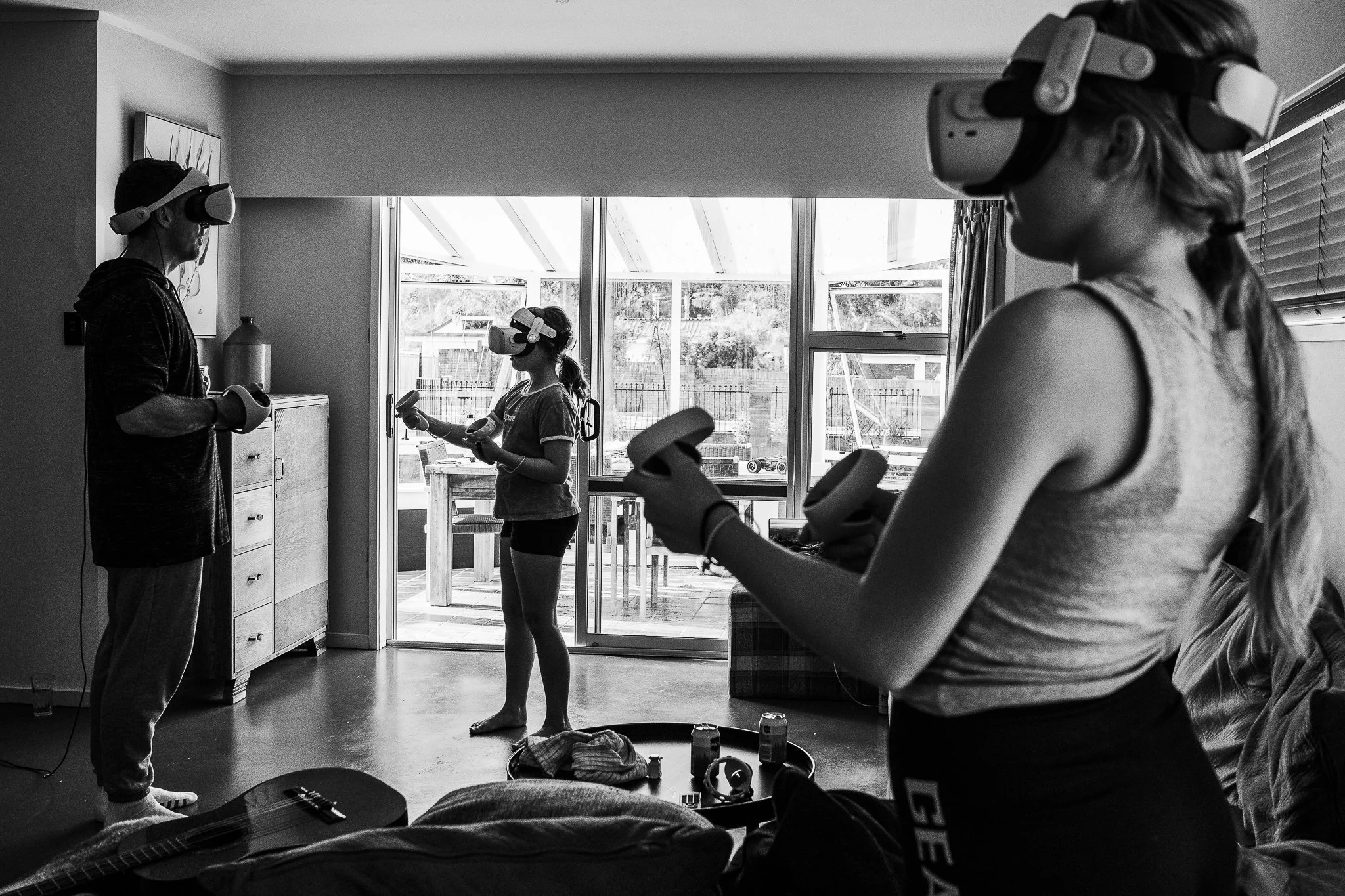 A family use VR headsets in their lounge, photographed in black and white with layers, by Natalia Byrdie Auckland documentary photographer