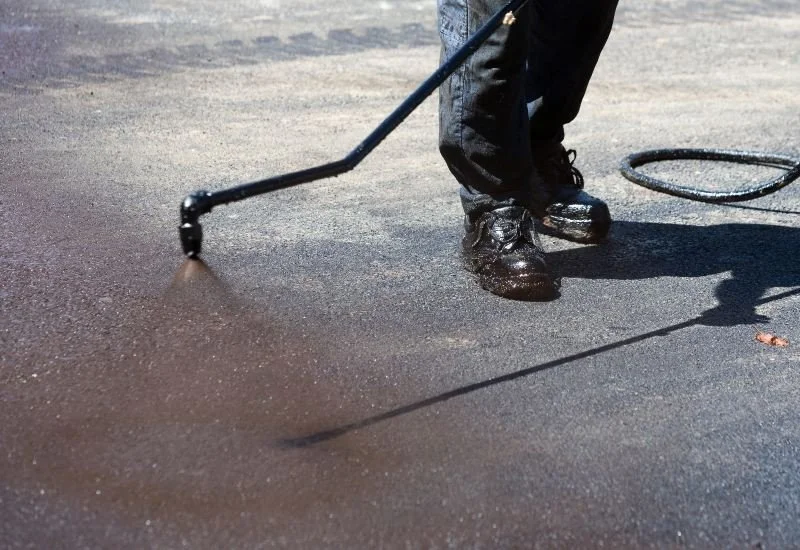 Person using a power sander on asphalt surface.