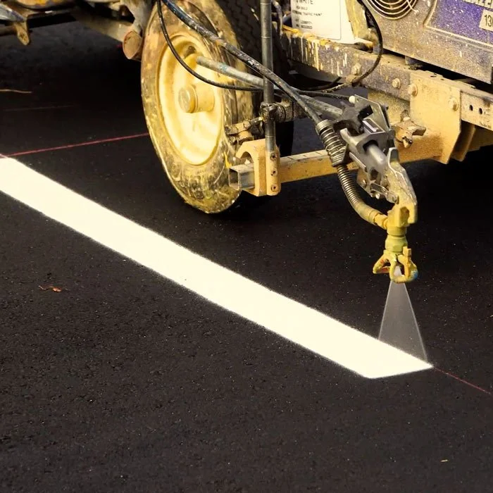 A paving machine spraying white asphalt onto a road surface.