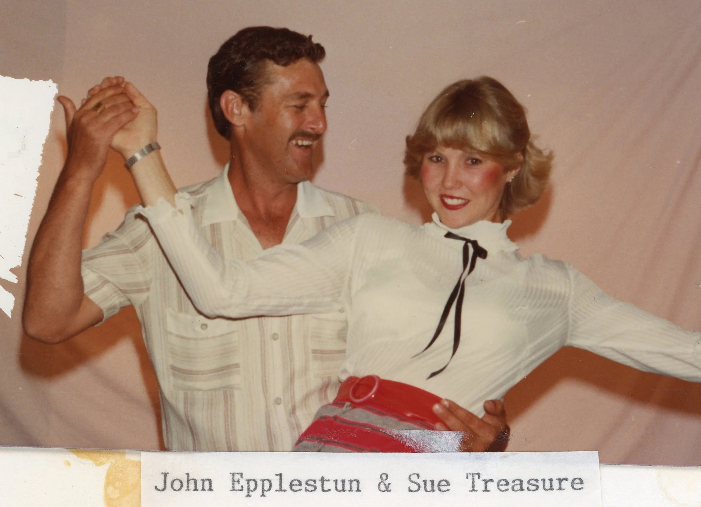 John Epplestun and Sue Treasure dancing together, smiling, with Sue wearing a white blouse with ruffles and a red skirt with a belt.