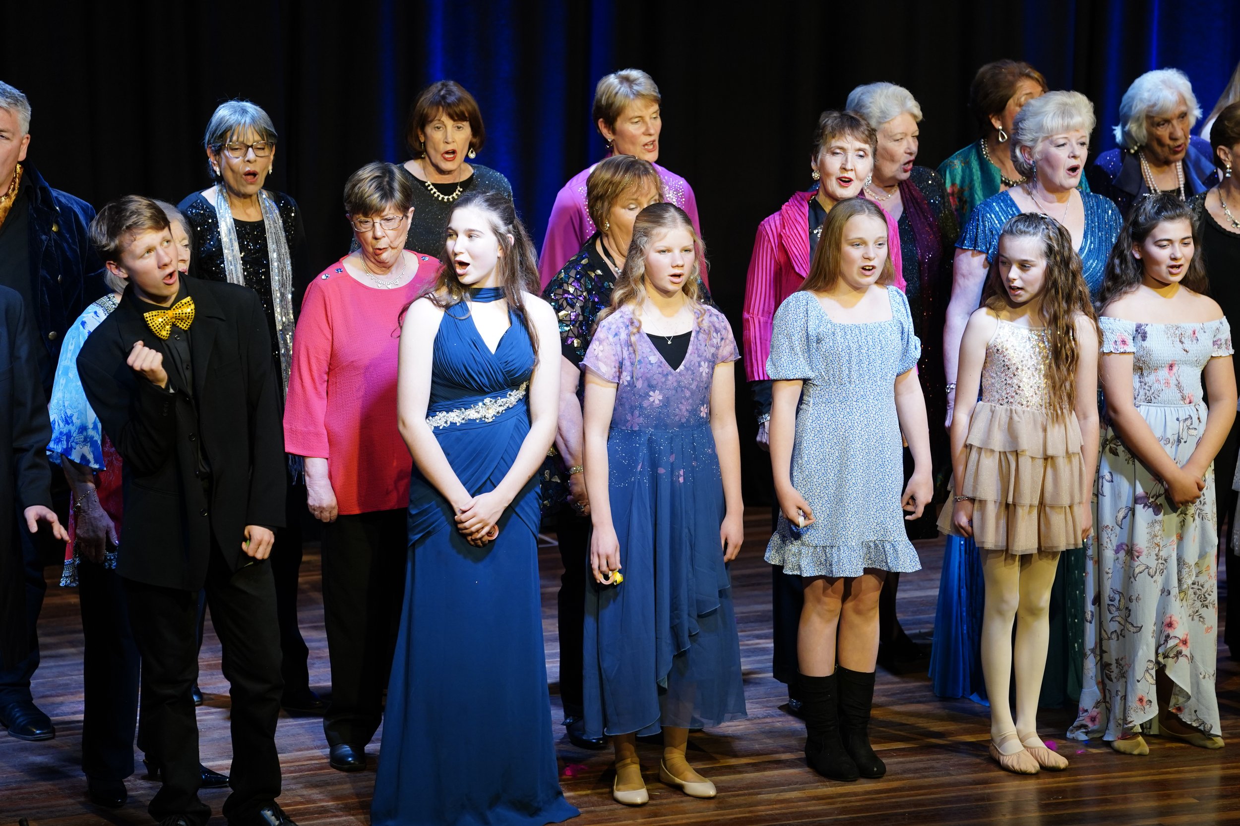 Group of children and adults singing on stage during a concert or performance.