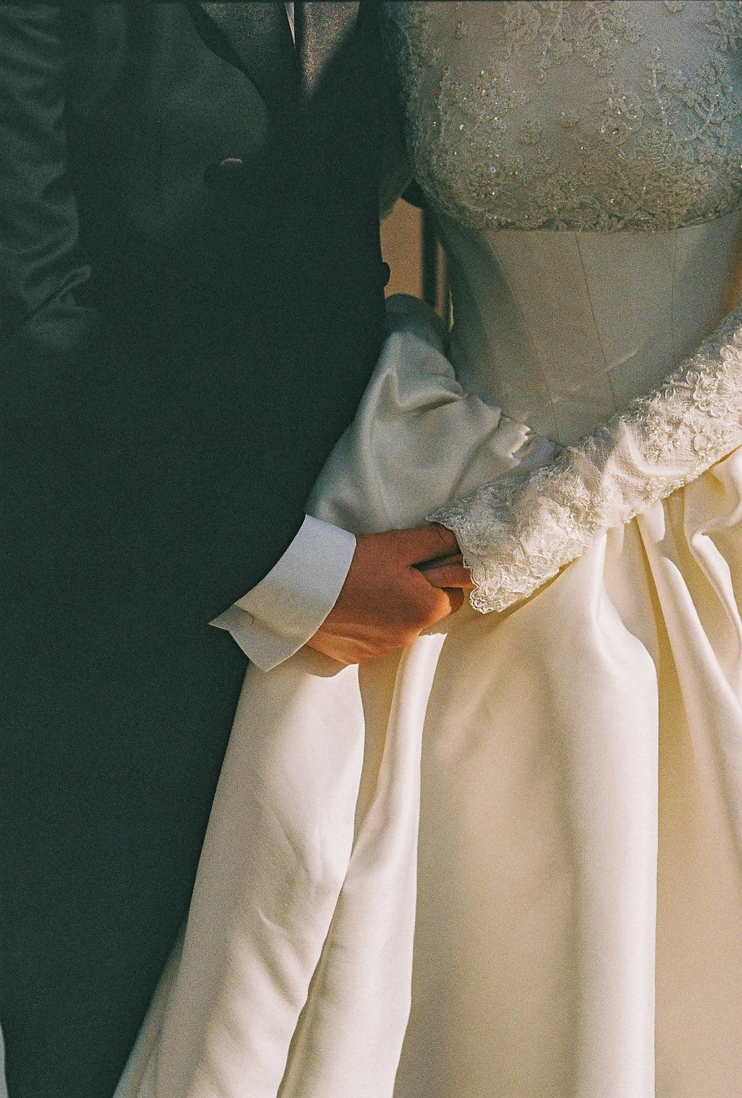 Close-up of a wedding cake with a bride and groom's hands holding each other, on a table with decorative fabric and a silver cake topper.