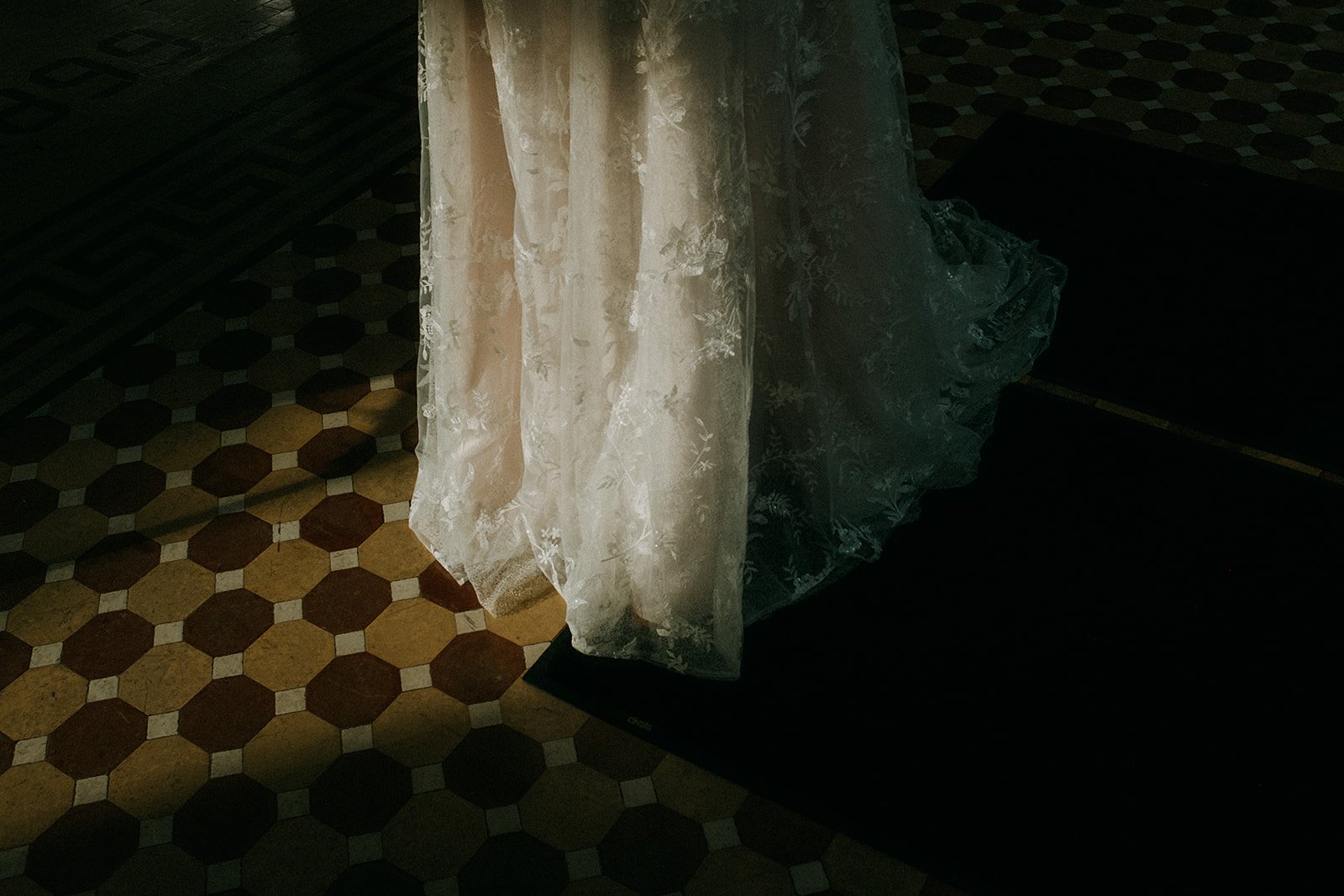 A lace curtain hanging in front of a black piece of furniture, with a patterned tile floor visible to the left.