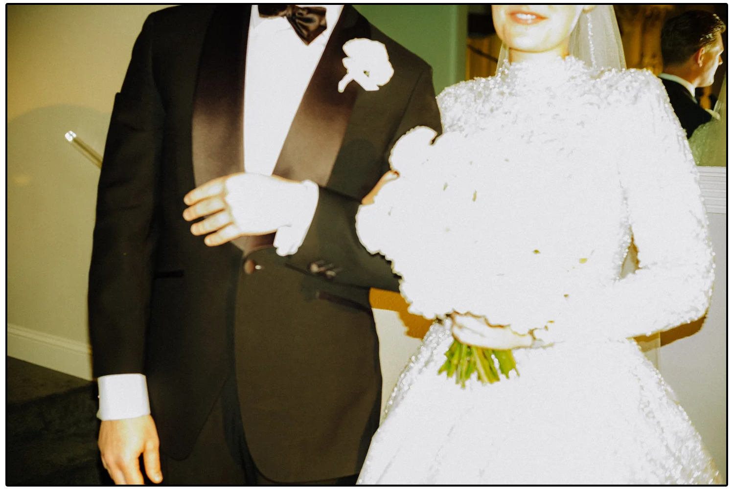 A bride in a white wedding dress holding a bouquet of white flowers and a groom in a black tuxedo with a white shirt and black bow tie at their wedding celebration.