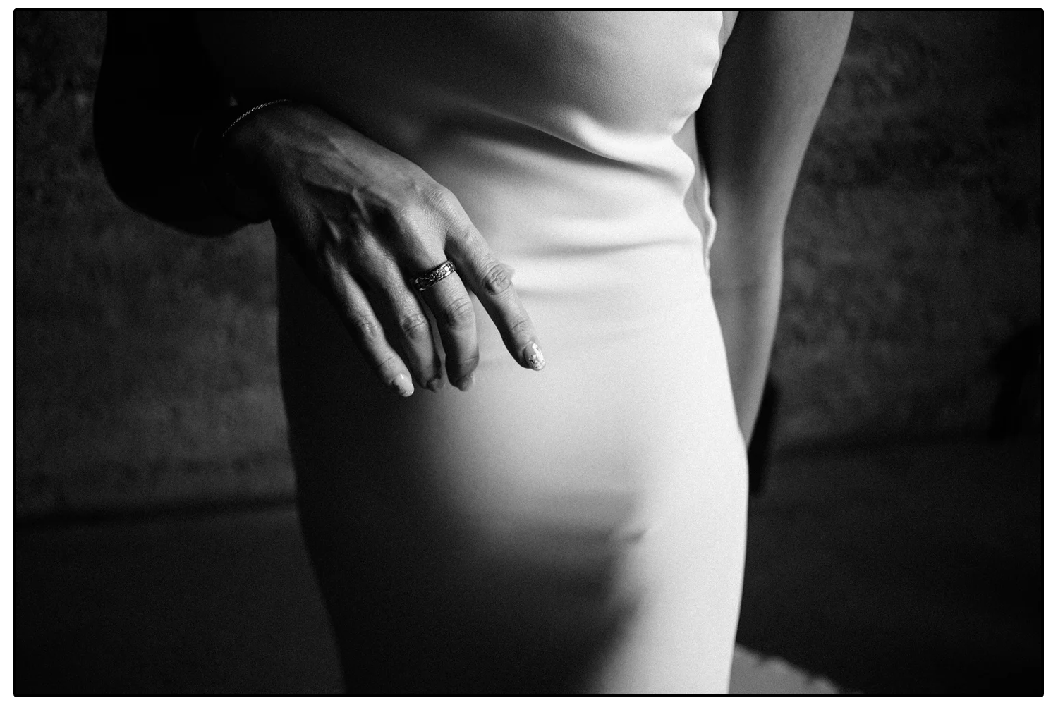 Close-up of a woman's hand resting on her hip, wearing a ring, with her body partially visible in a fitted white dress.