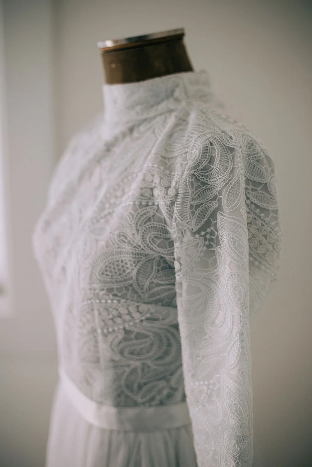 Close-up of a dress form wearing an elegant white lace dress with intricate floral embroidery.