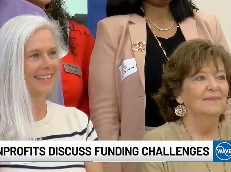 Amy Meredith, UP for Women and Children Executive Director, being interviewed at an event with people mingling and tables in the background.
