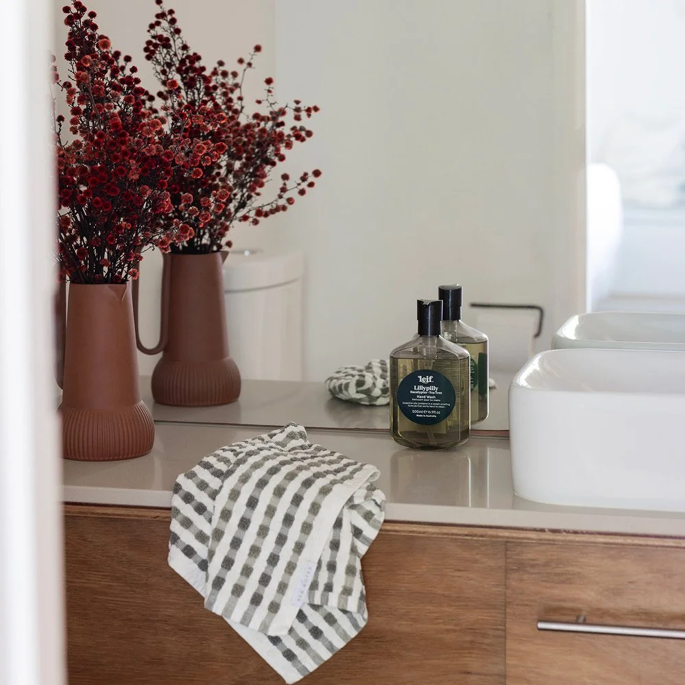 A bright vase of red flowers beside a hand basin and hand towel