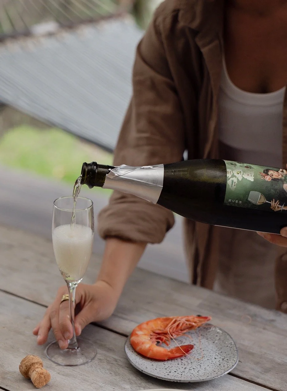 Detail of a female guest pouring sparkling wine with a Yamba prawn on a plate 