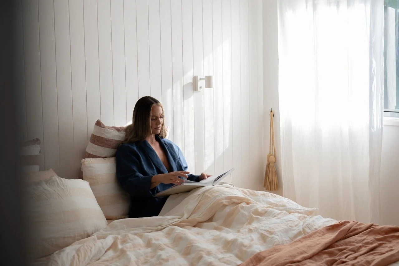 Female guest relaxing in navy robe in bed with book in sun-filled room
