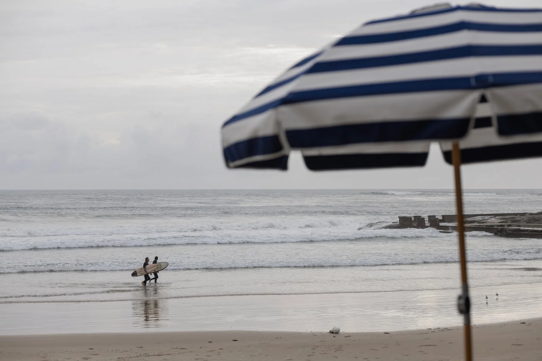 Two surfers leaving the water at Main Beach with the kiosk umbrellas in the foreground