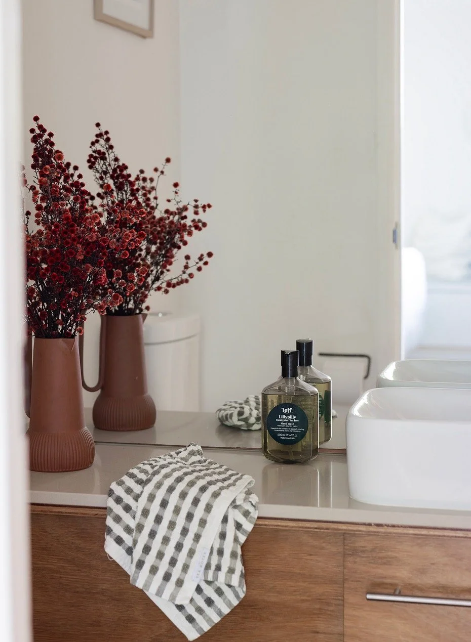 Vibrant red flowers in rust-coloured ceramic vase in powder room with Leif hand soap and draped hand towel