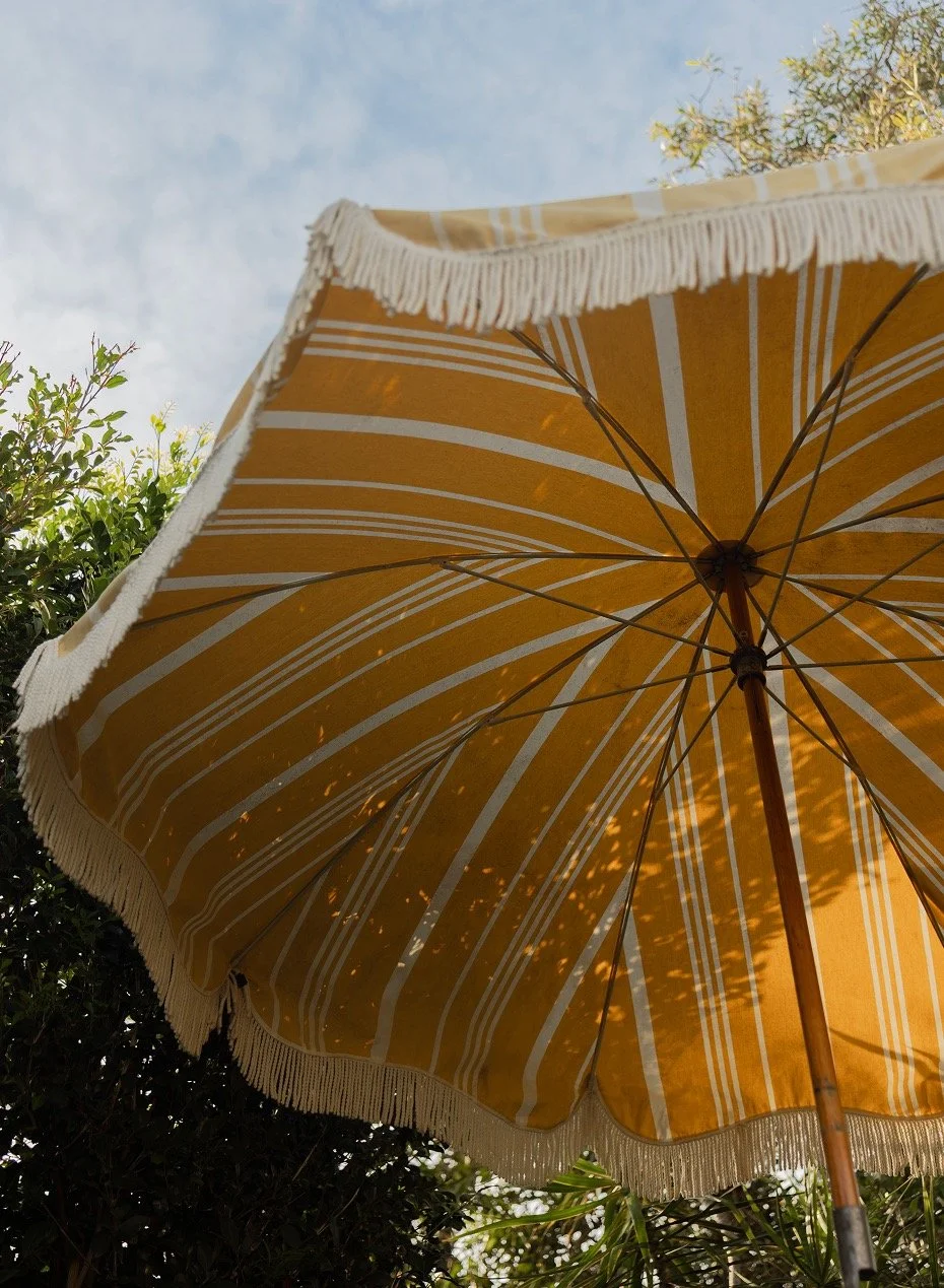 Fringed yellow-striped umbrella in garden with dappled light canopy