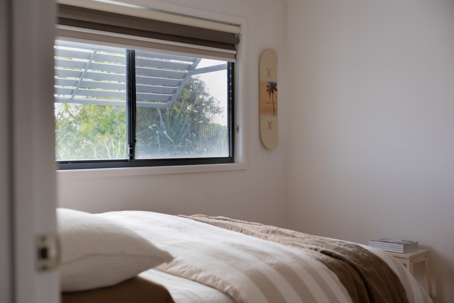 Striped French linen bedding with decorative skateboard on wall, and greenery through window 
