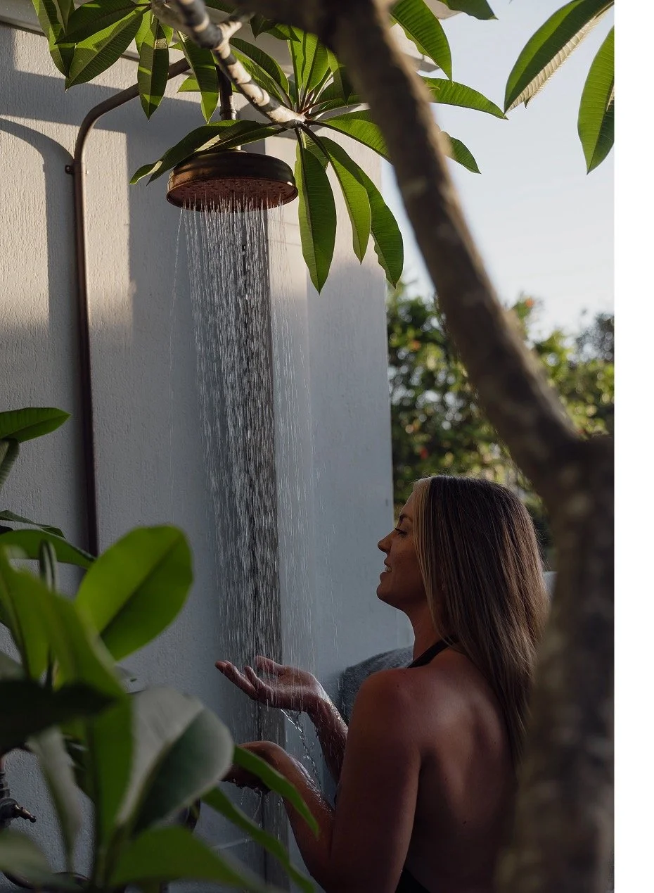 Female guest in swimsuit beneath hot/cold outdoor shower and frangipani tree