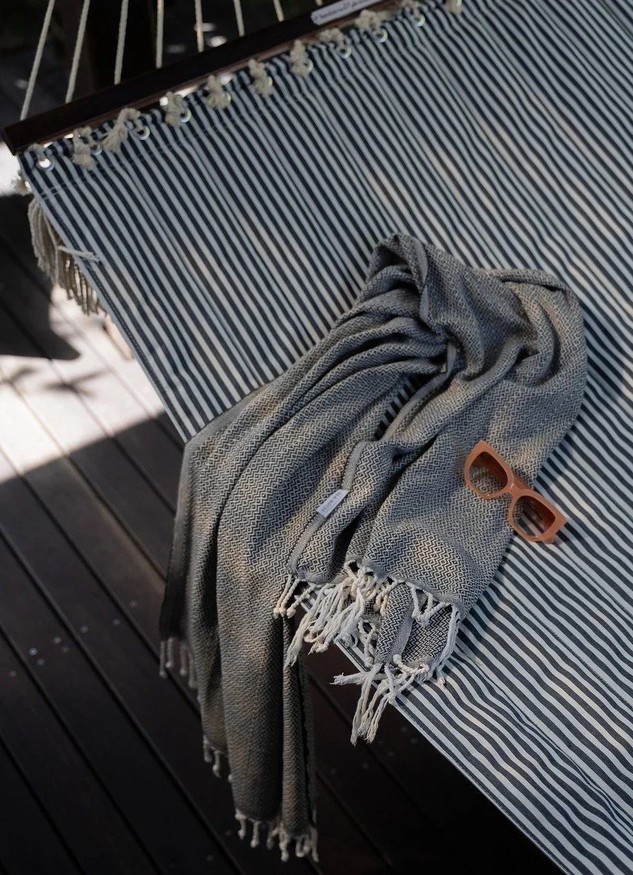 Turkish beach towel and sunglasses draped on striped canvas hammock