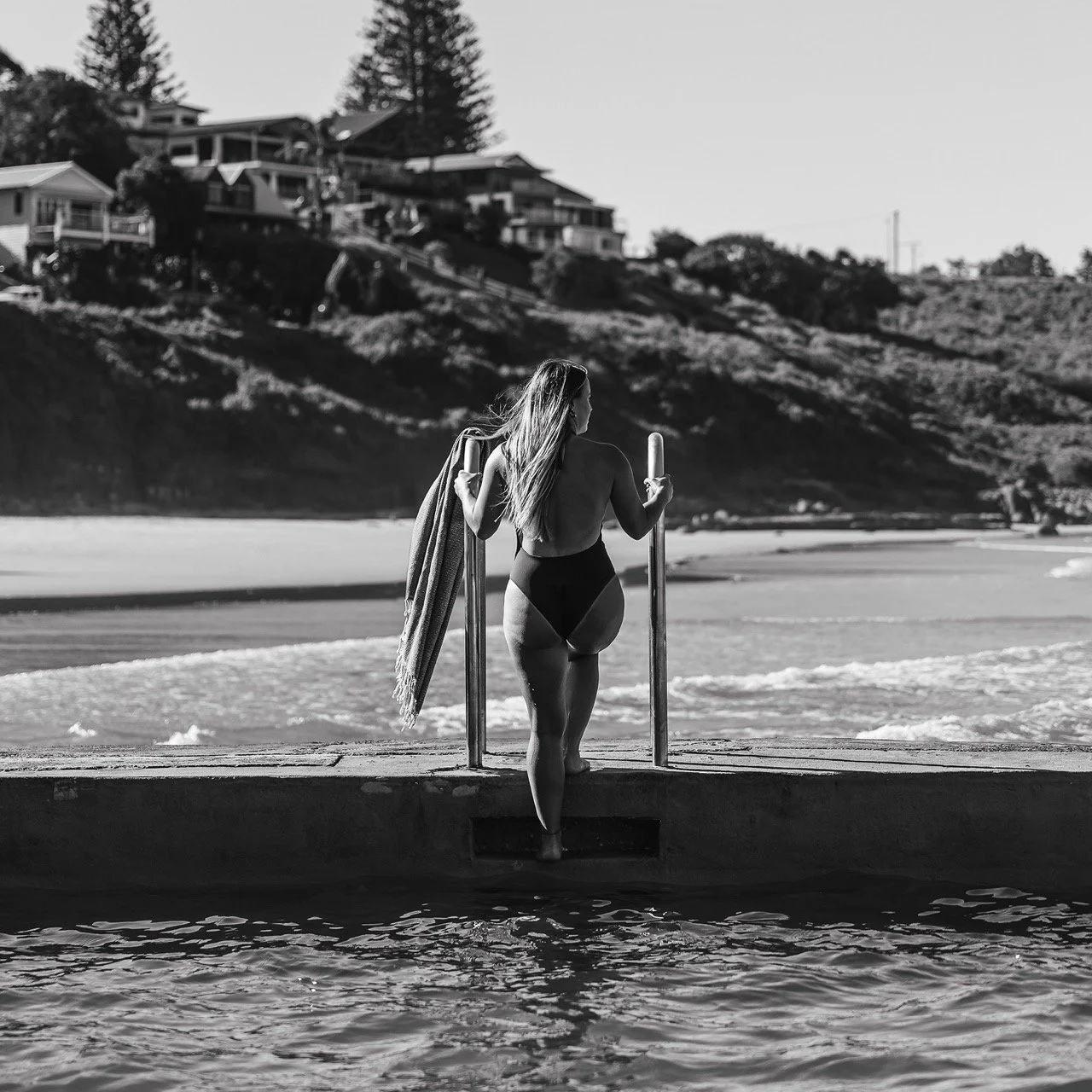 Female guest lowering herself into ocean baths down the ladder overlooking main beach
