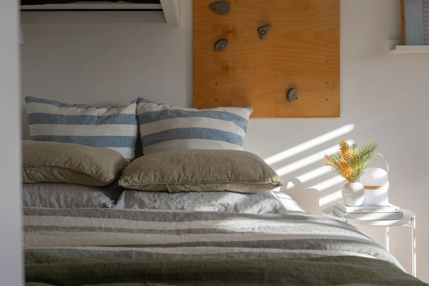 Close up of Queen bed with a climbing wall up to the top bunk, bedside table with native flowers and a small reading lamp 