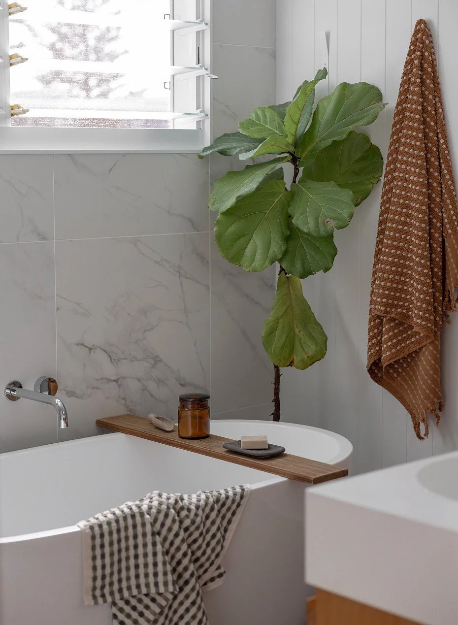 Light airy bathroom, freestanding bathtub beneath open louvre window, soft towels draped
