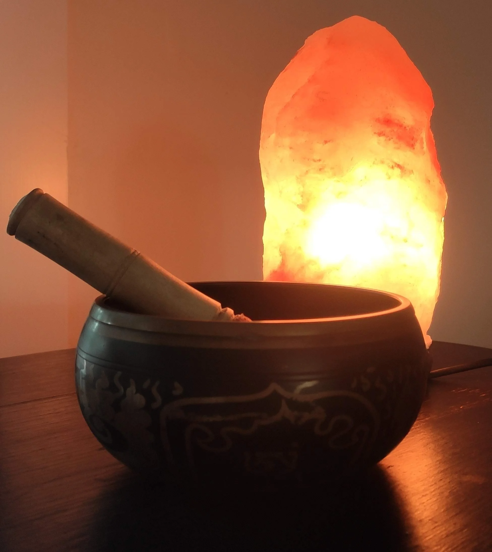 Salt lamp behind a ceramic bowl with a stick or incense stick inside, placed on a wooden surface.