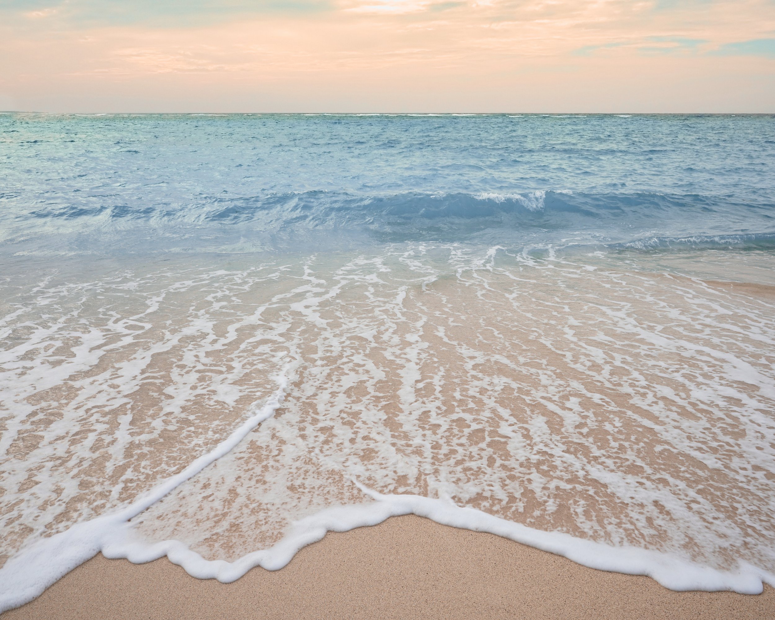 Calm ocean waves gently washing onto a sandy beach during twilight.
