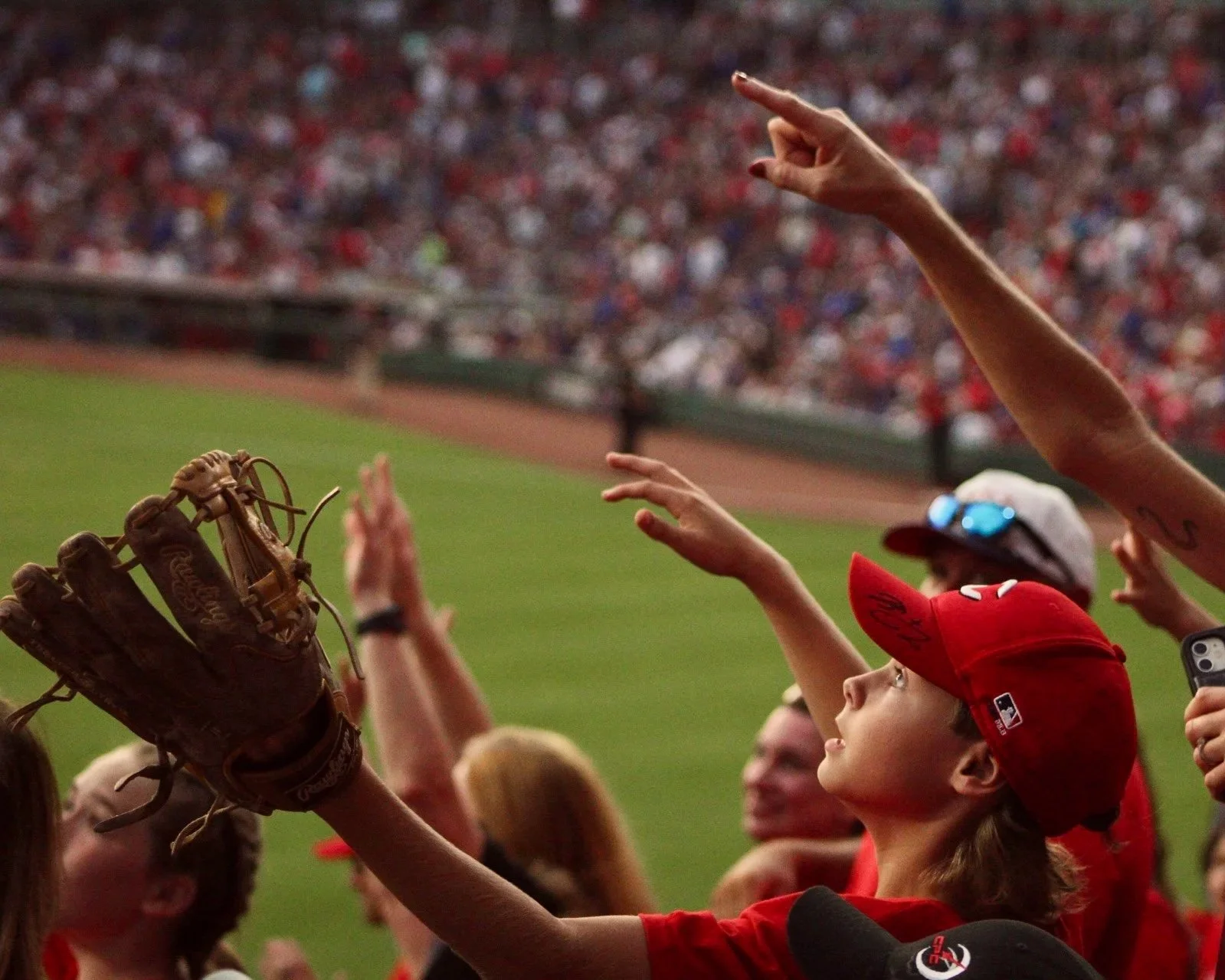 Young baseball fan in red cap reaching out with a glove during a game.