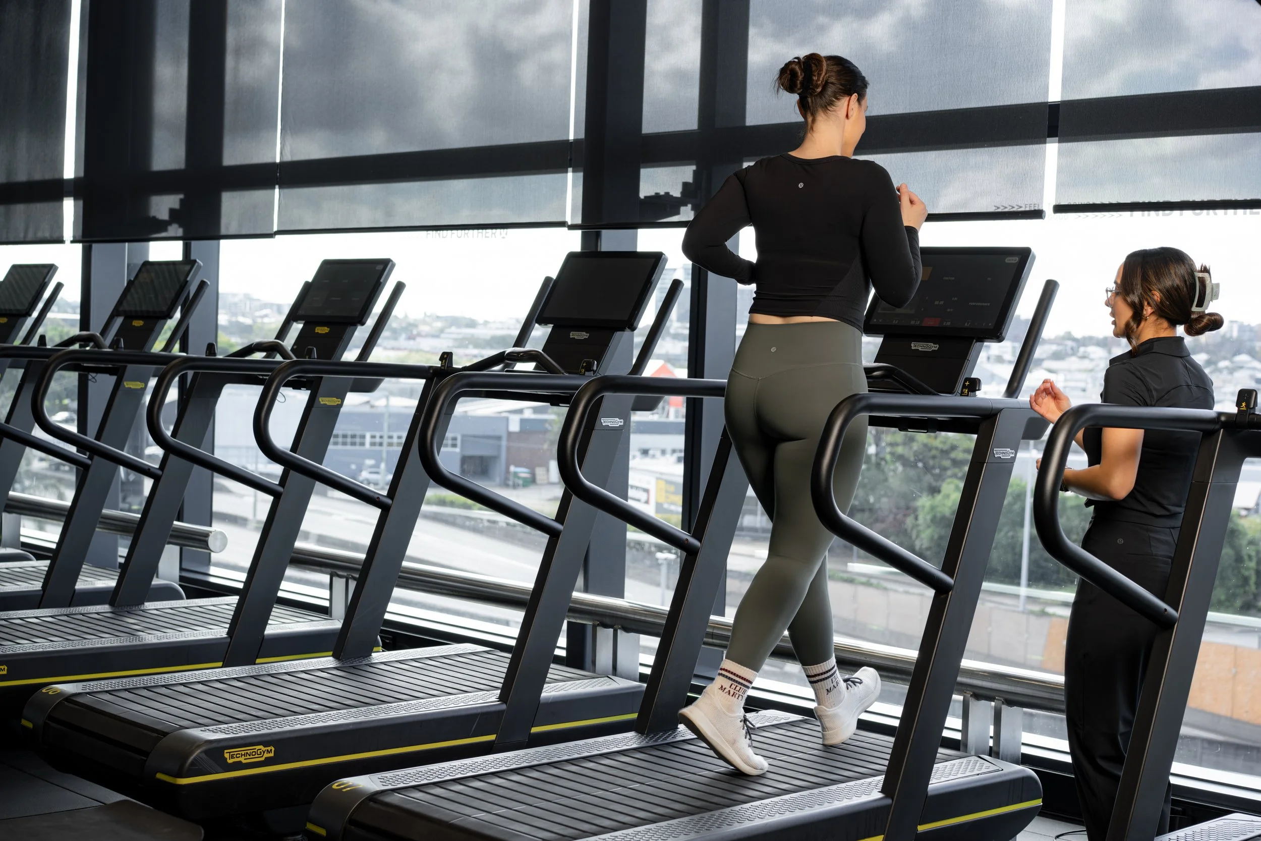 A woman performing a stretching exercise on a reformer machine in a gym.