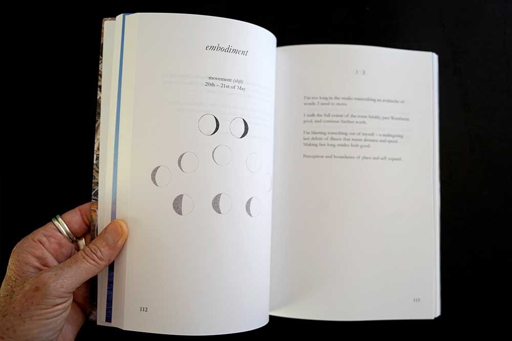 Open book showing a section titled 'embodiment' with moon phase illustrations and a paragraph of text on the right page.