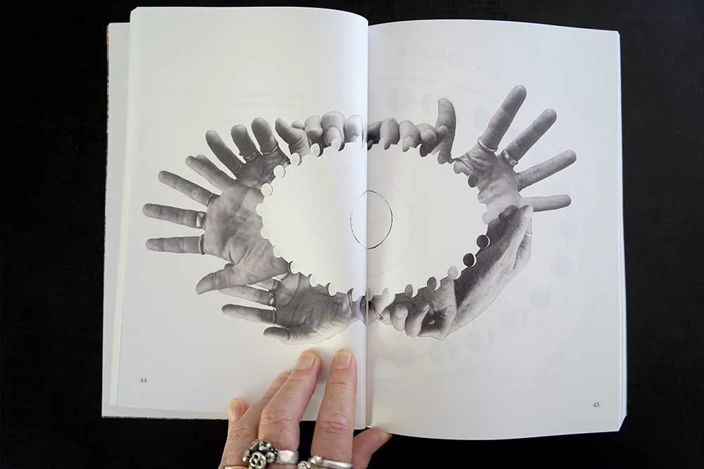 Open book showing black and white cutout image of multiple hands forming a heart shape.