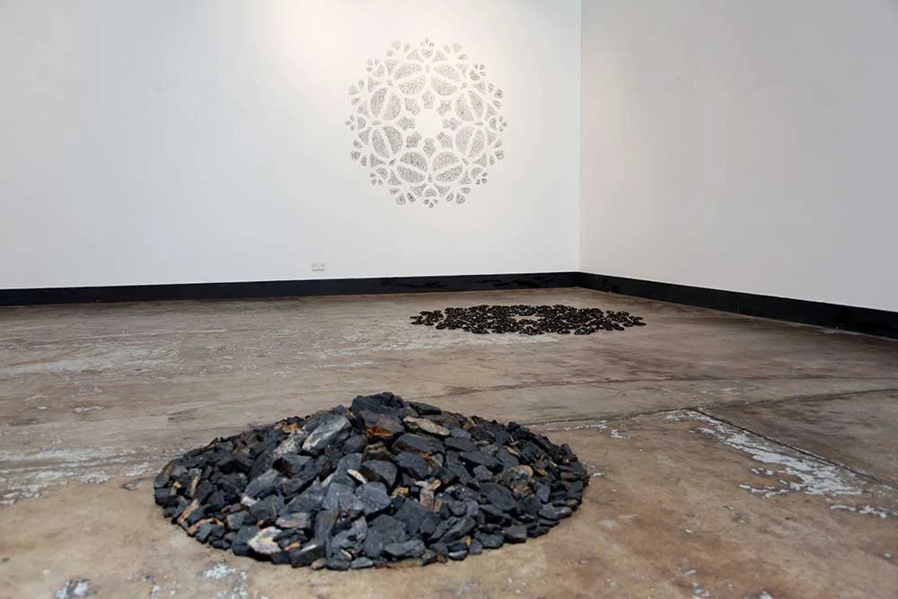 Installation view: Turning of the Tide (at 1.03 metres high), coal collected from landslip, 1.03m diameter; High Tide, New Moon, 7 April 2019, sea-washed coal pebbles & sea ephemera, 1.64 m diameter; & Remnant, coal markings (on wall), 1.64m diameter