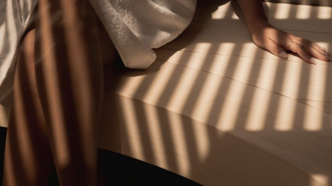 A person's hand resting on a wooden surface with shadows of blinds cast over it, sunlight streaming through.